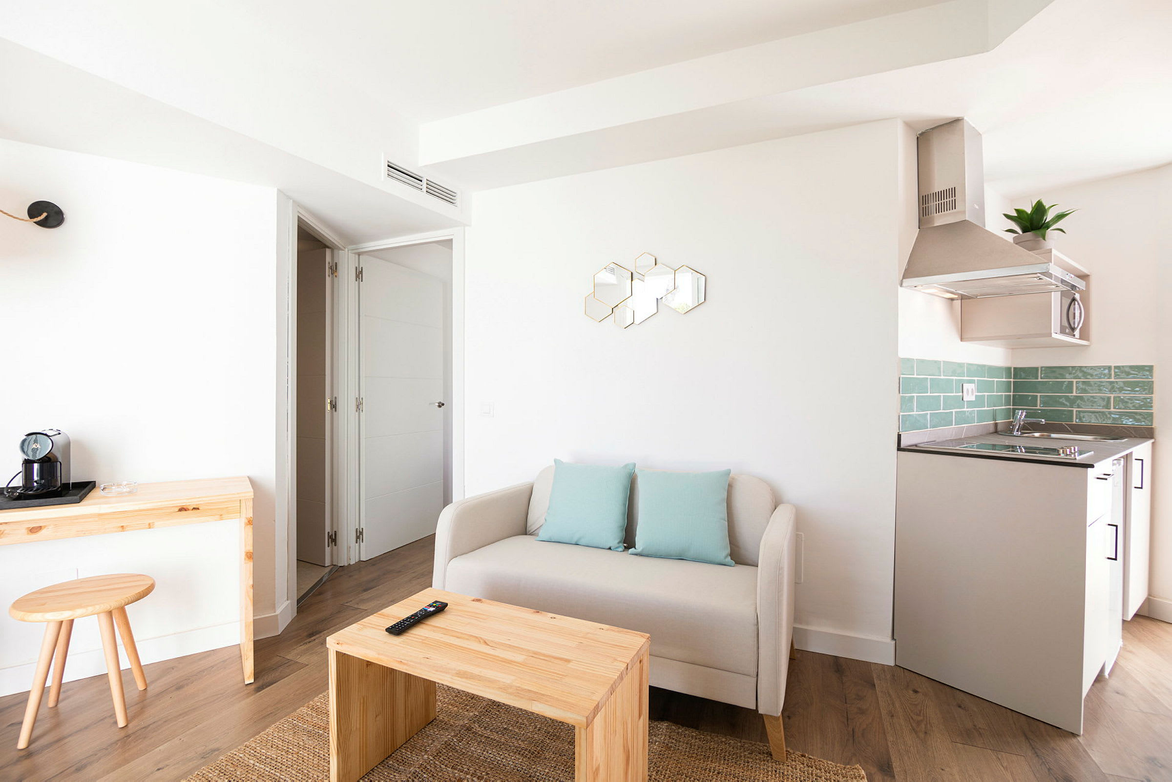 Moderne innredet stue med beige sofa, trebord og et lite kjøkkenområde med grønne fliser. (AI-generert tekst)