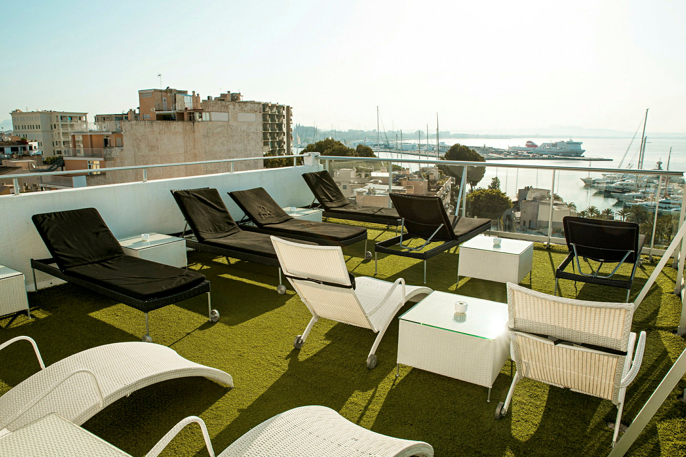 Utendørsområde med solsenger og bord på en terrasse med utsikt mot en havn. (AI-generert tekst)