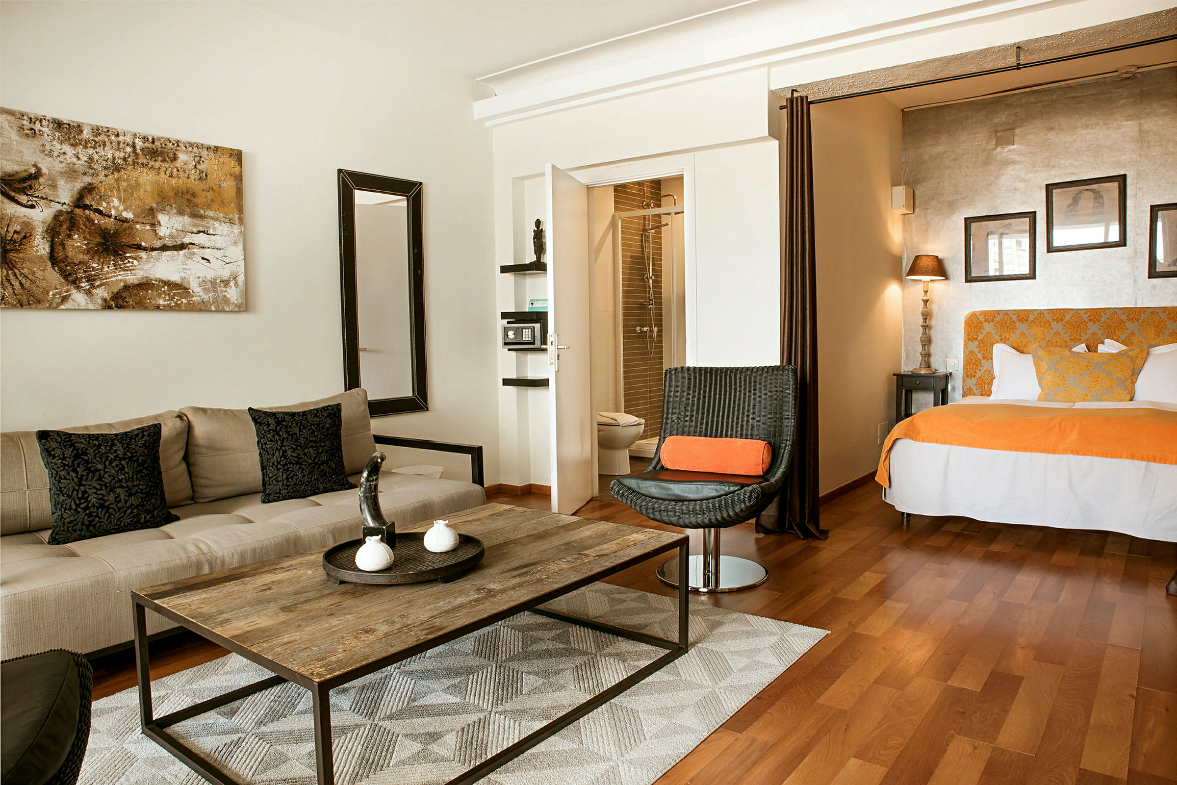 Et hotellrom med sittemøbler, et bord og en seng med oransje detaljer. (AI-generert tekst)