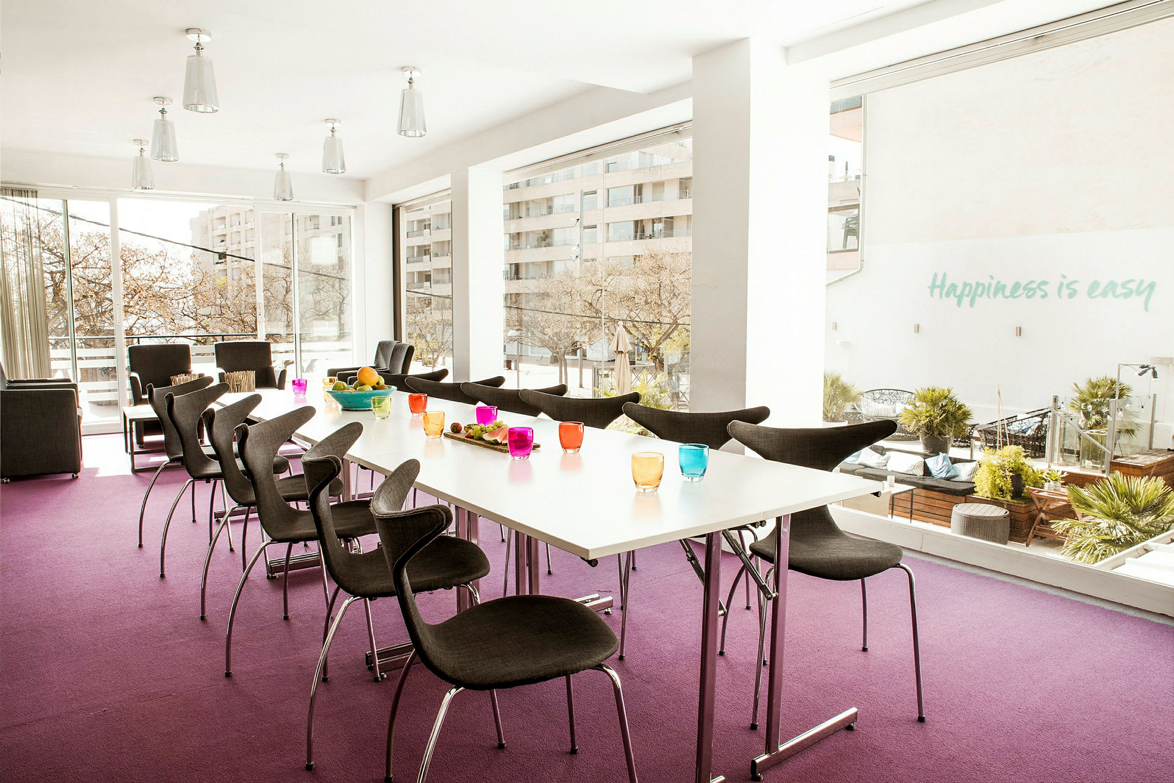 Et lyst, moderne konferanserom med store vinduer, bord med fargerike glass og mørke stoler. (AI-generert tekst)