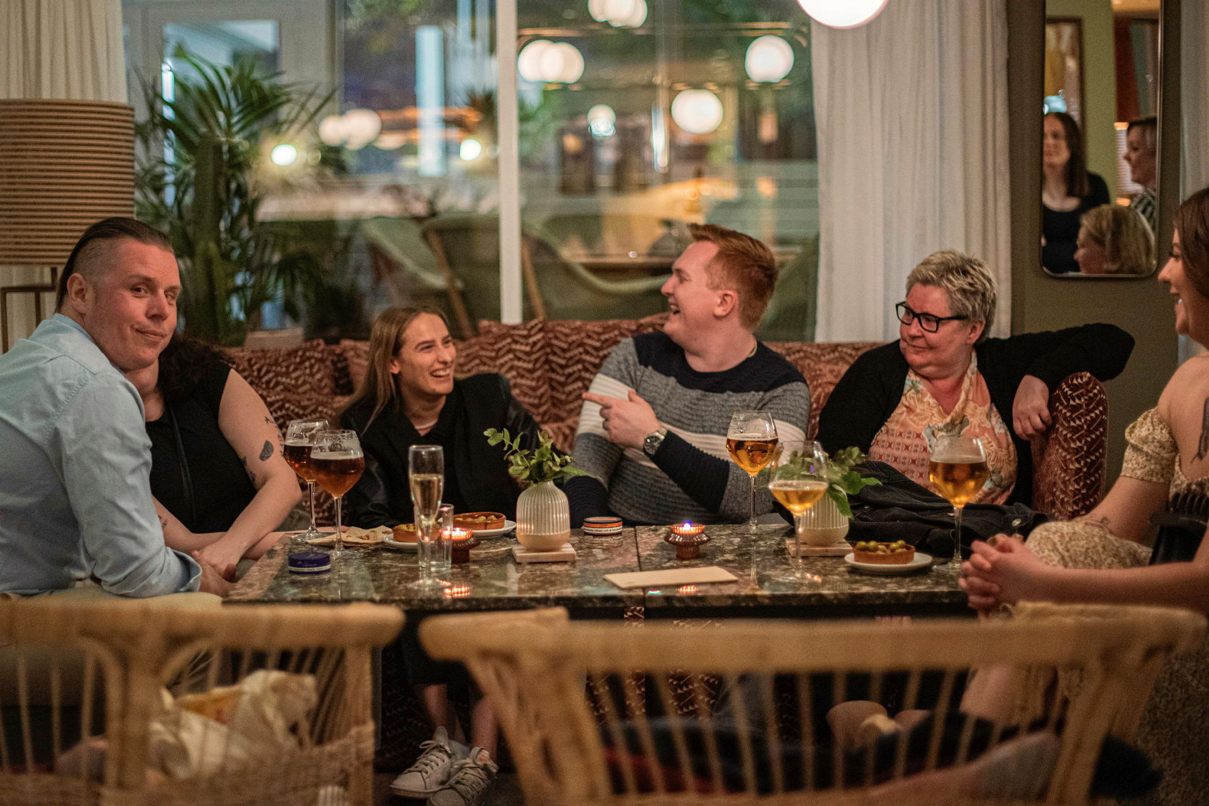 Folk sitter ved et bord med drikke og matbiter på en restaurant. (AI-generert tekst)