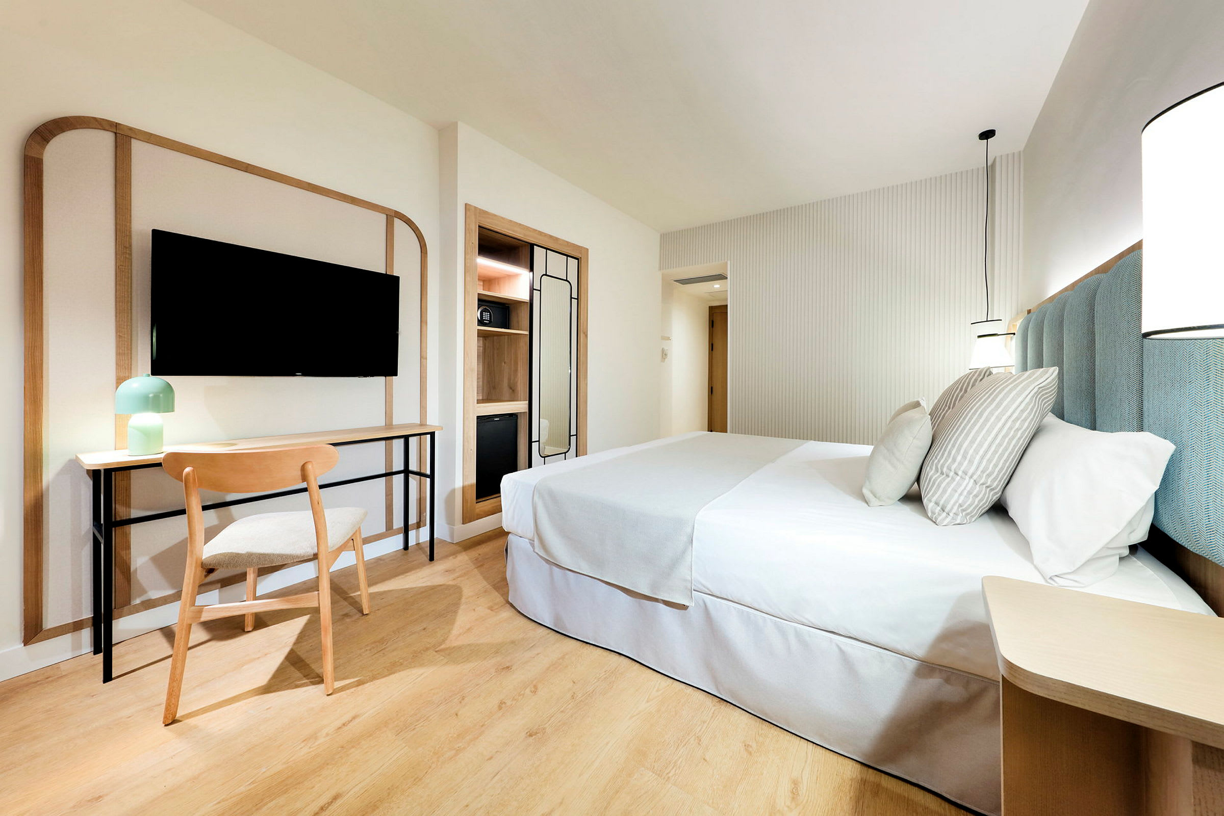 Et moderne og lyst hotellrom med en dobbeltseng, skrivebord og stol, samt en veggmontert TV. (AI-generert tekst)