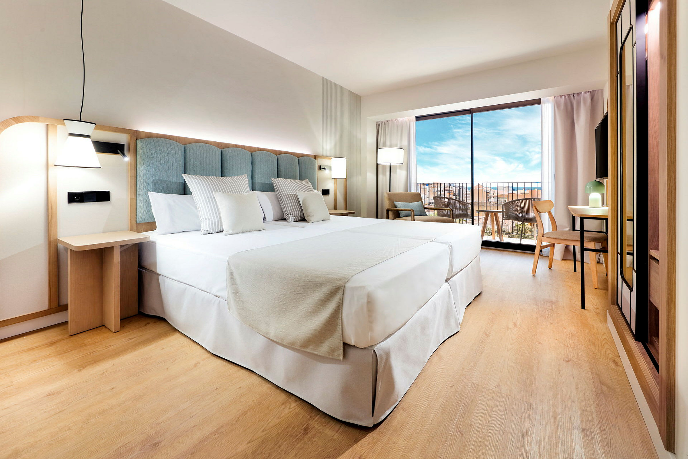 Et hotellrom med en stor oppredd seng, paneler i lyst tre, og et stort vindu som viser en utsikt utendørs. (AI-generert tekst)