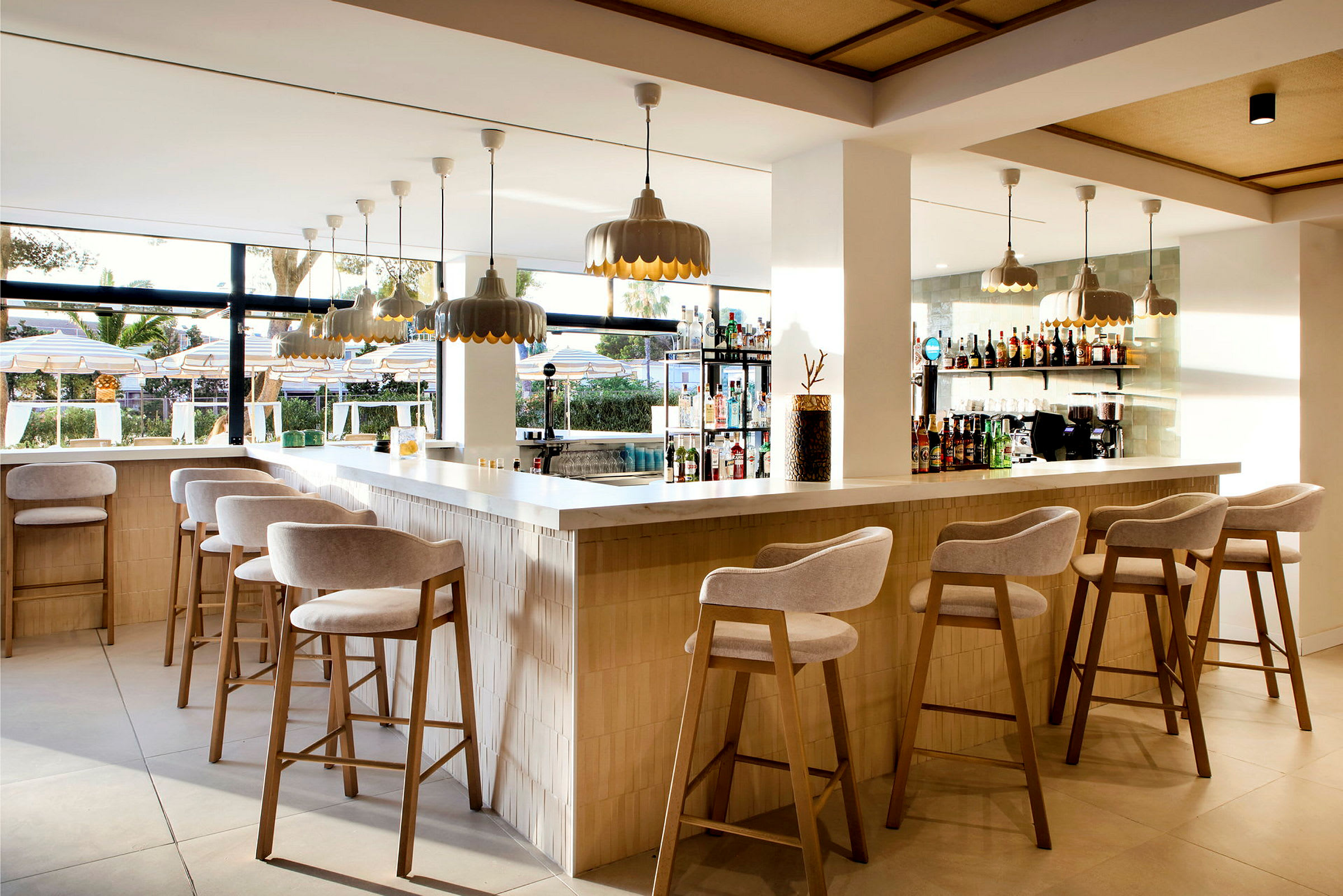 En moderne bar med barstoler, hengende lamper og utsikt mot et utendørsbasseng. (AI-generert tekst)