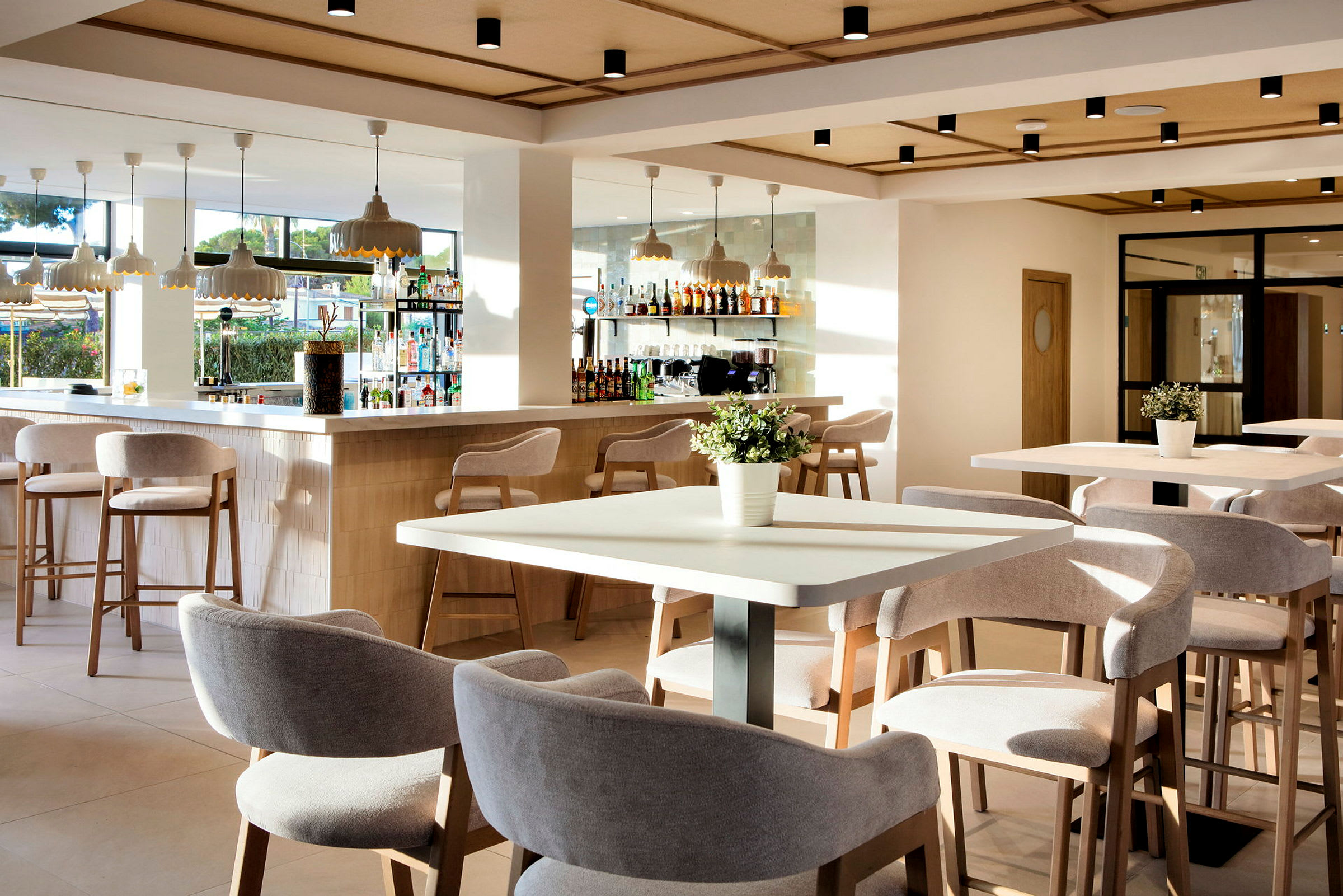 En lys og moderne bar og restaurant med sitteplasser ved bord og bar, samt dekorative detaljer som blomsterpotter. (AI-generert tekst)