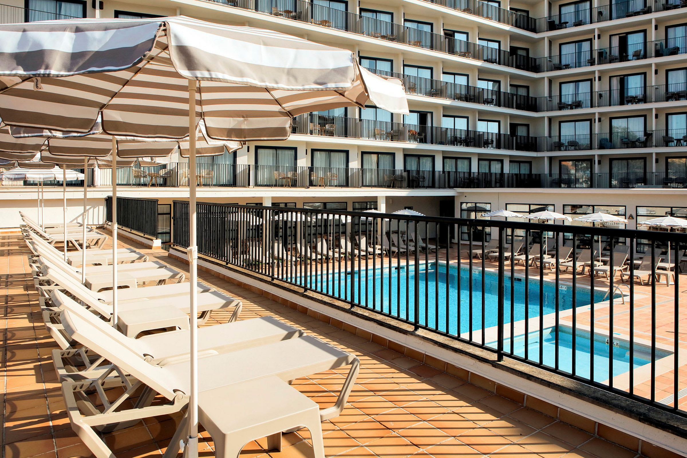 Utsikt over hotellbassengområde og solsenger med parasoller. (AI-generert tekst)