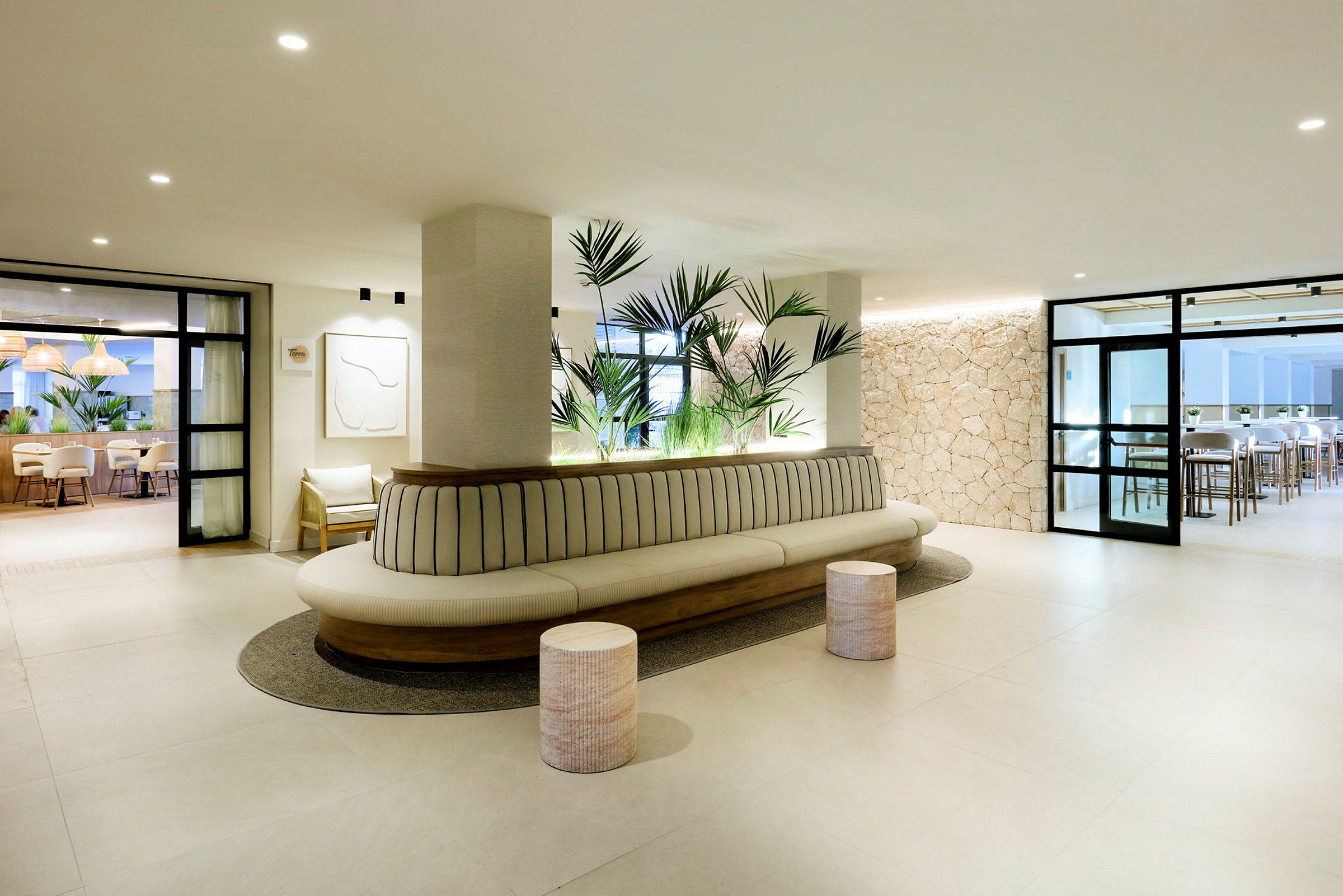En moderne lobby med lys innredning, en lang sofa med planter bak og stoler samt bord i bakgrunnen. (AI-generert tekst)