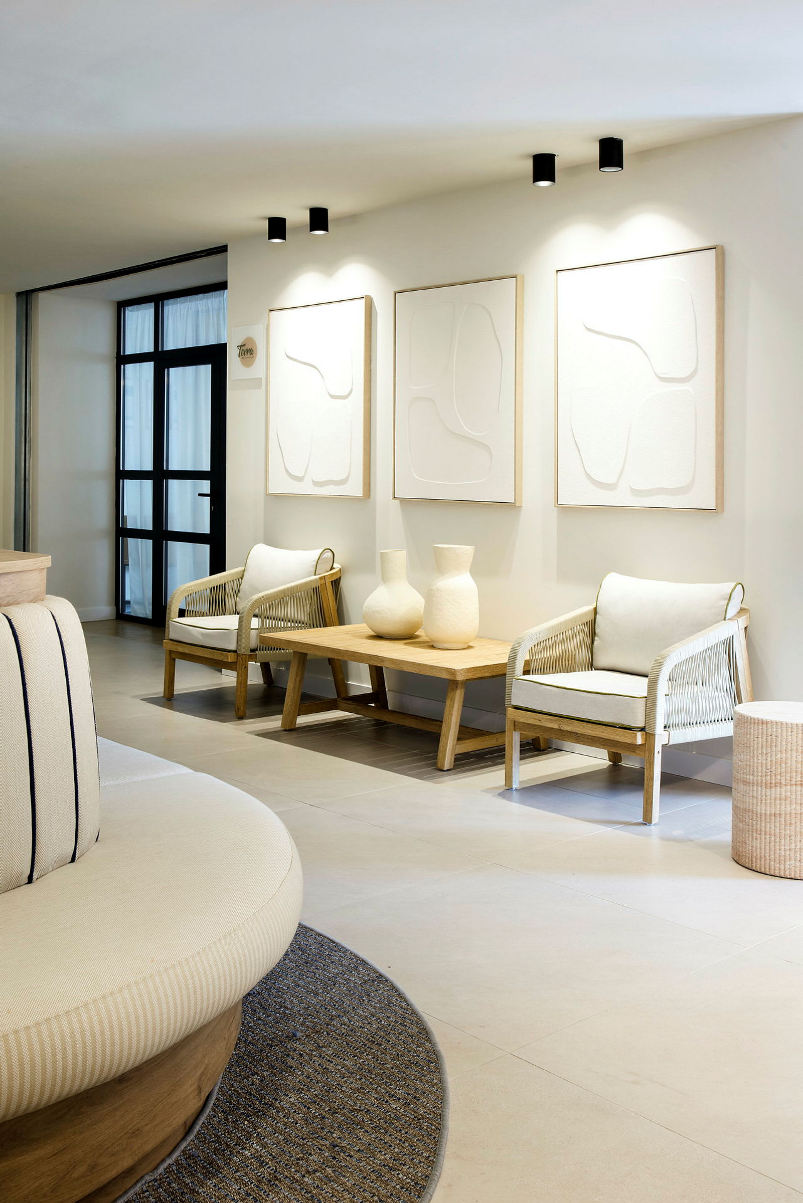 Et moderne og elegant loungeområde med to lenestoler, et trebord med to dekorative vaser og tre minimalistiske malerier på veggen. (AI-generert tekst)