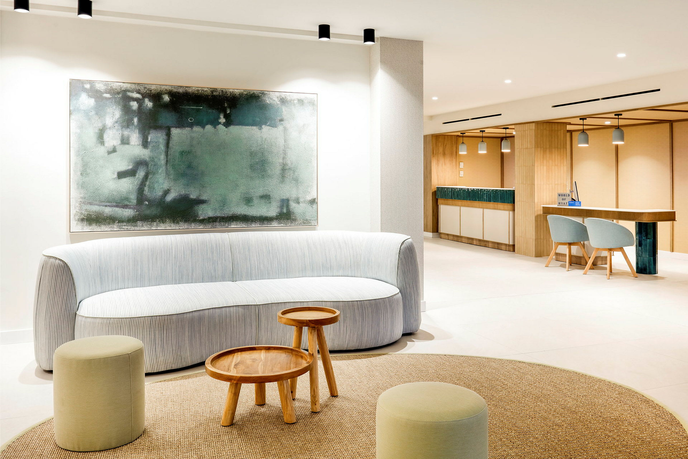En lys, moderne lounge med en sofa, små trebord og krakker. Et stort abstrakt bilde henger på veggen bak sofaen. (AI-generert tekst)