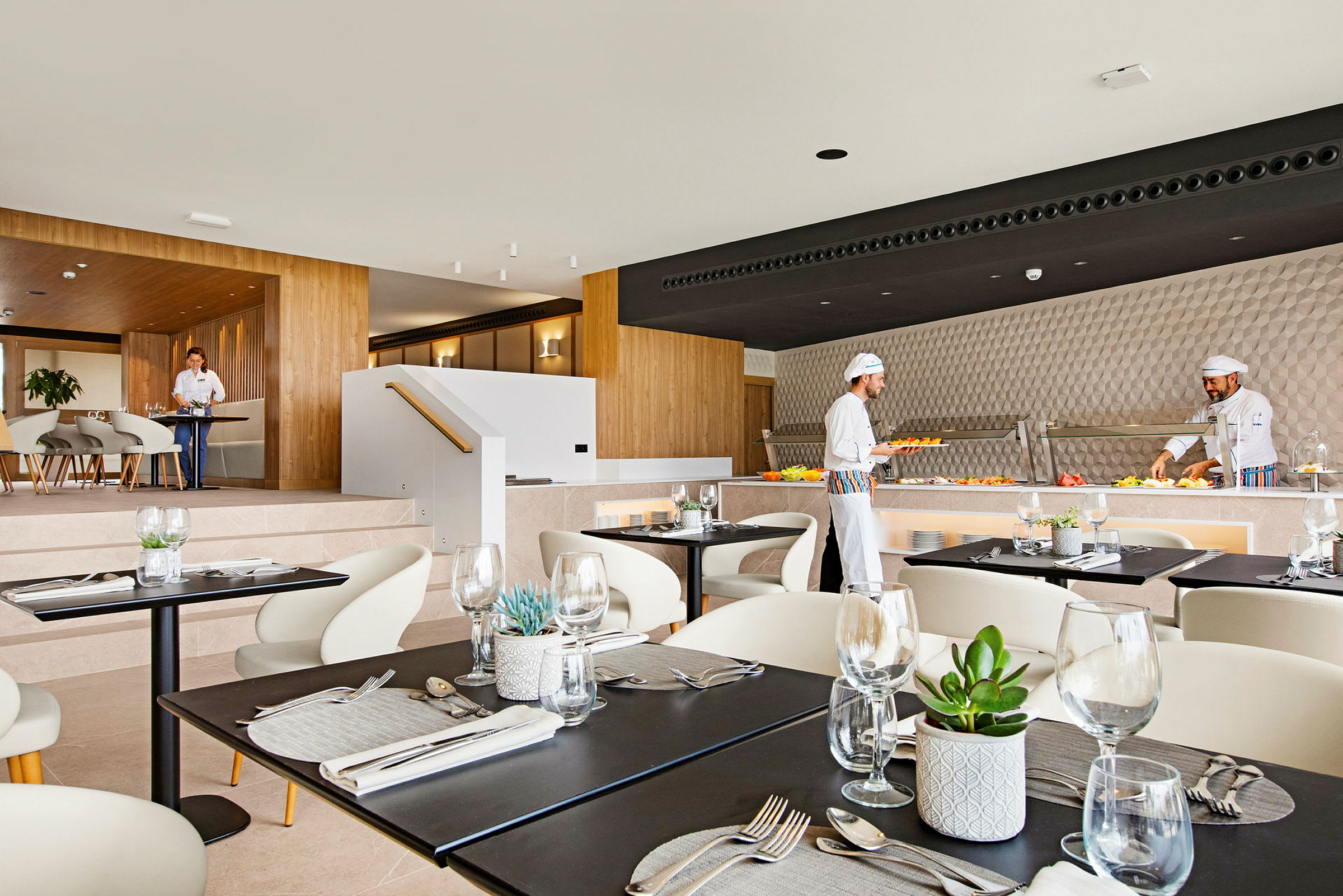 En moderne restaurantinteriør med dekkede bord. Kokker tilbereder mat ved en buffé. (AI-generert tekst)