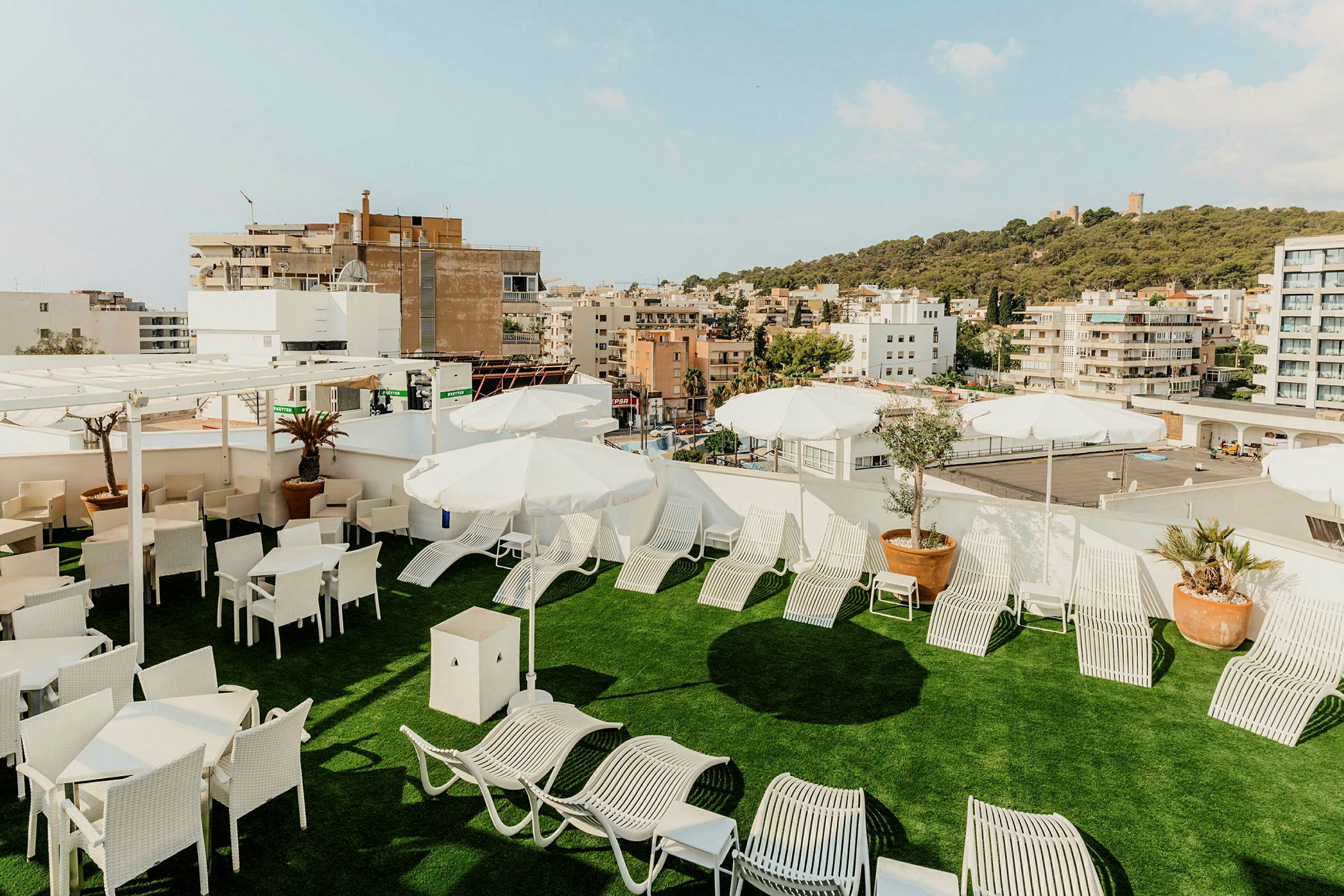 Takterrasse med solsenger, parasoller og sittemøbler. Utsikt over byen og en grønn ås. (AI-generert tekst)