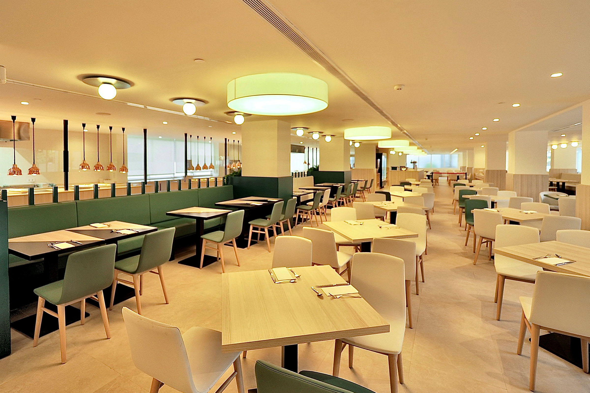 En lys og romslig restaurant med moderne møbler og belysning. Bord og stoler er plassert i jevne rekker. (AI-generert tekst)