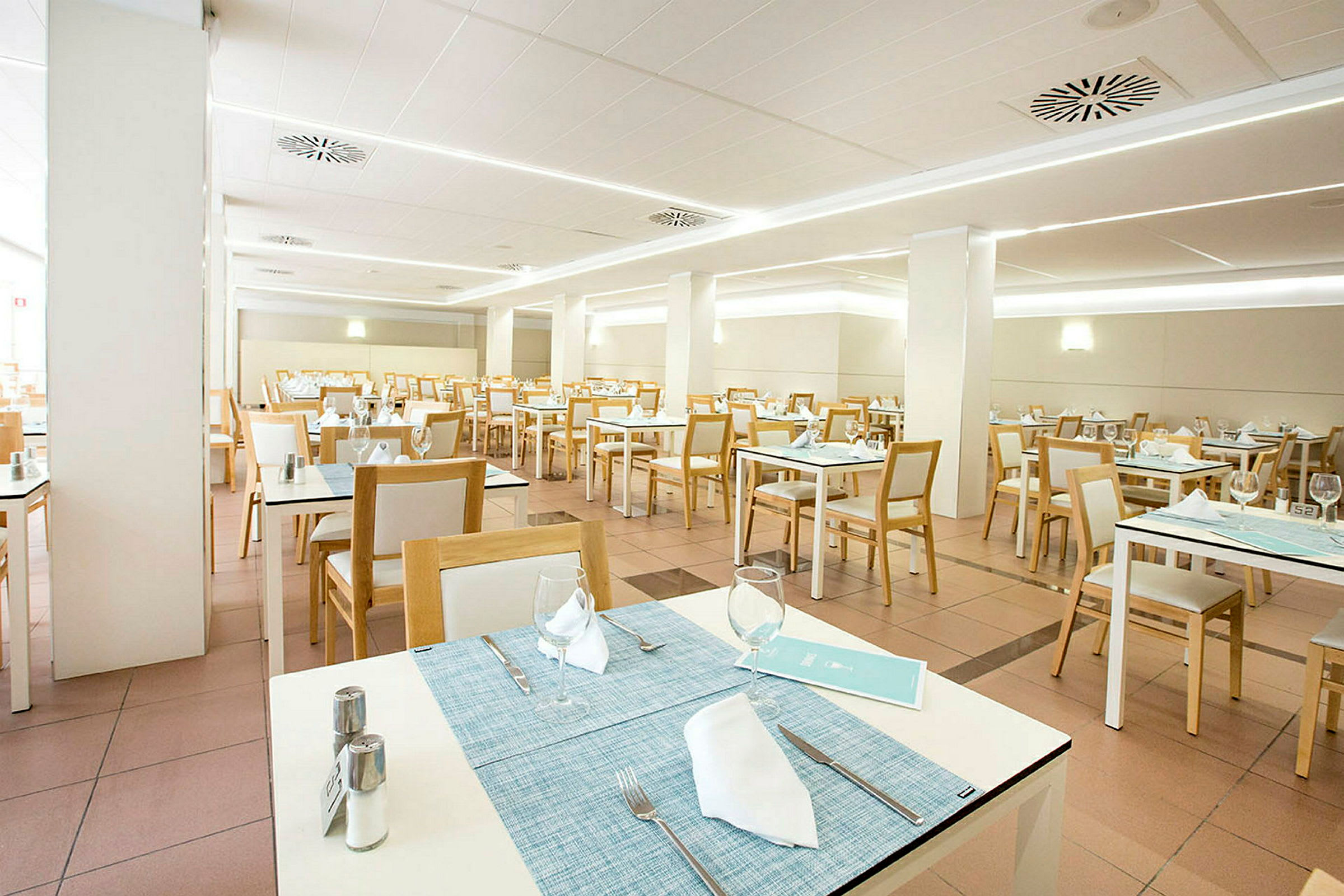 En lys og moderne restaurant med hvite bord og trestoler, dekket for gjester. (AI-generert tekst)