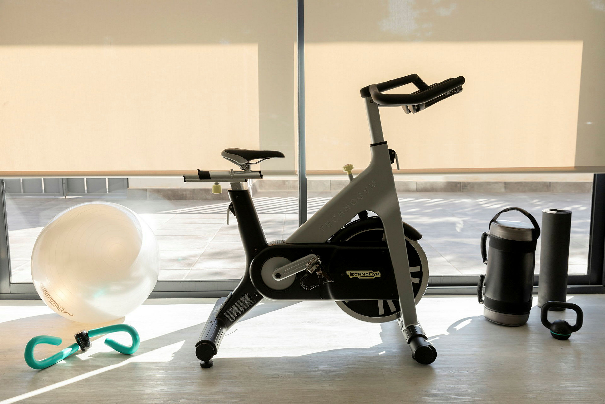Et treningsrom med en treningssykkel, en treningsball, en vannflaske, en yogamatte og en kettlebell. (AI-generert tekst)