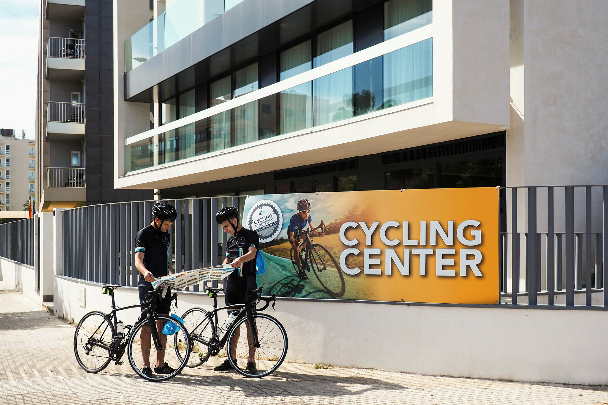 To personer står med syklene sine foran en bygning merket som Cycling Center. (AI-generert tekst)