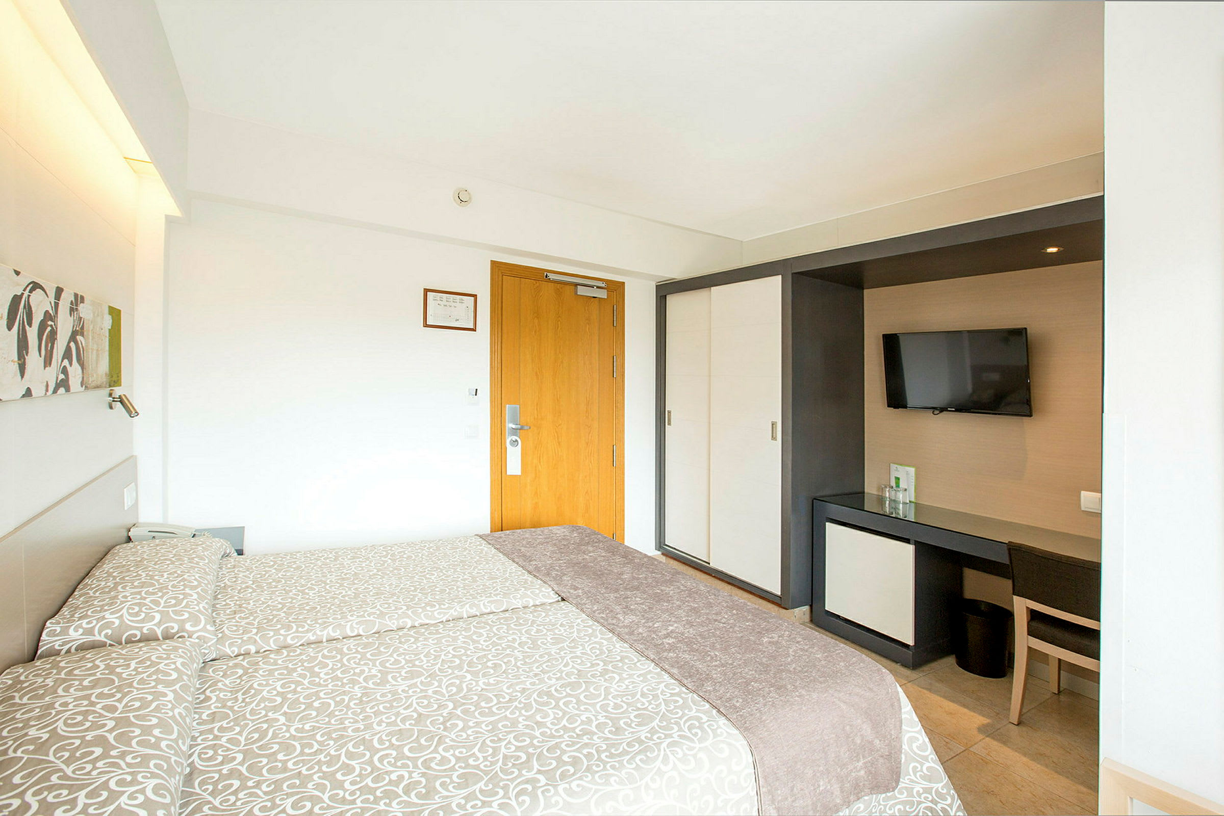 Hotellrom med to senger, TV og skrivebord. (AI-generert tekst)