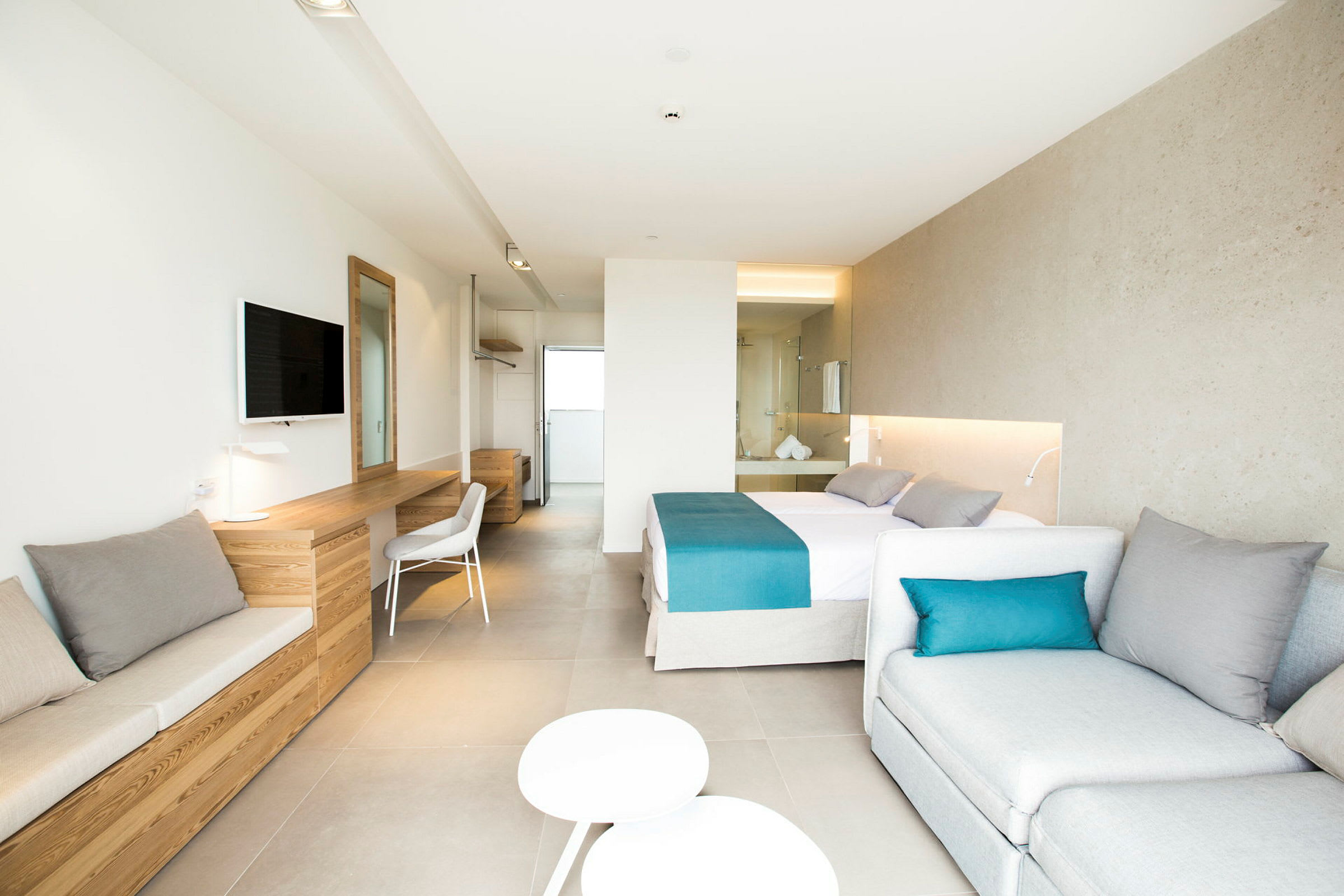 Et lyst hotellrom med dobbeltseng, sittemøbler, skrivebord og veggmontert TV. Rommet har moderne innredning og er godt opplyst. (AI-generert tekst)
