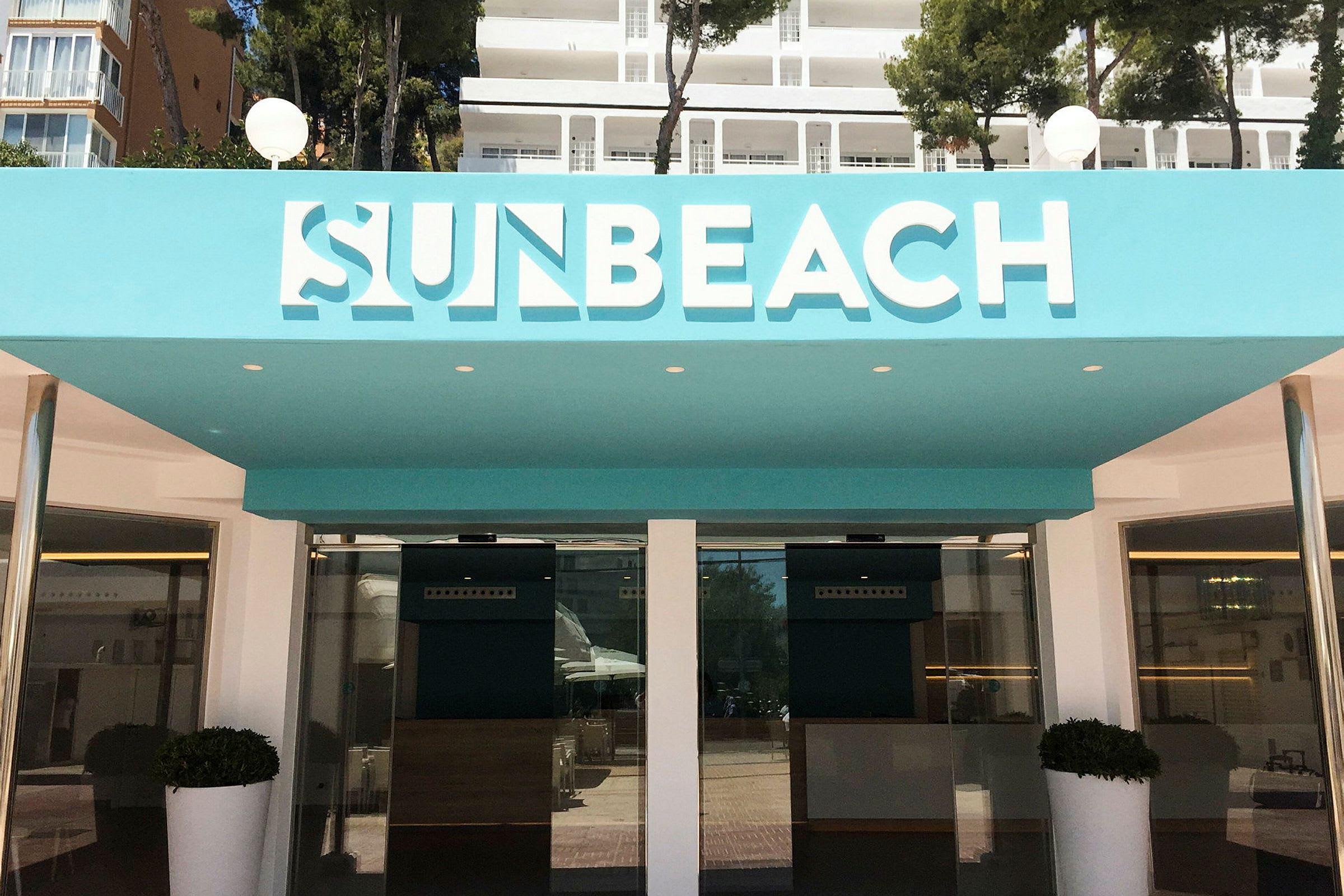 Inngangen til Sun Beach-hotellet med turkise detaljer. (AI-generert tekst)