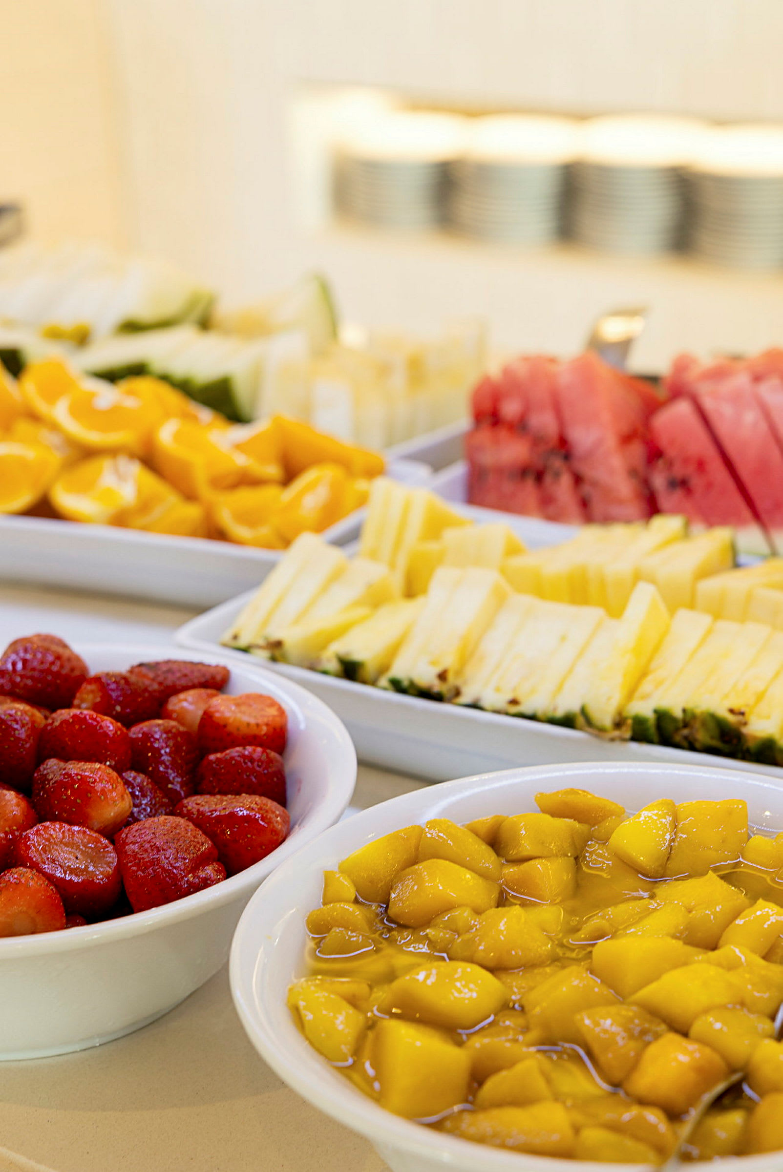 Oppskåret frukt, inkludert jordbær, mango, melon og ananas, servert i hvite boller. (AI-generert tekst)