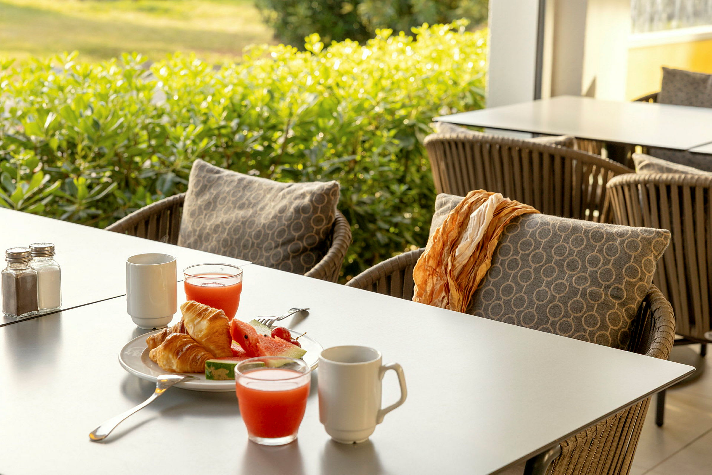 Frokost med croissanter, vannmelon og juice på et bord med utemøbler. (AI-generert tekst)