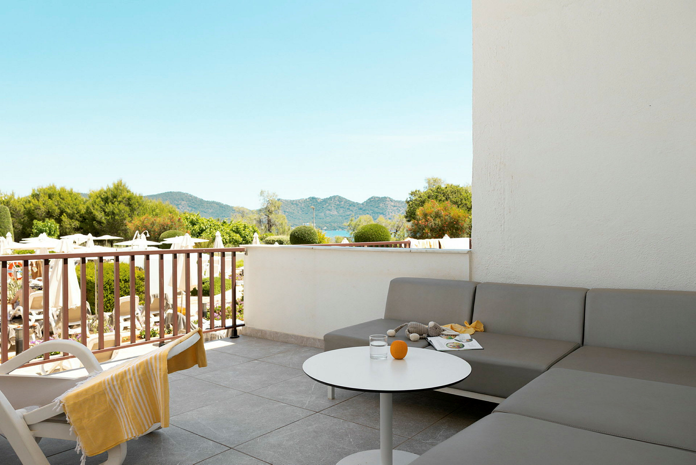 Terrasse med grå sofa, hvitt bord og utsikt over hage og fjell. (AI-generert tekst)