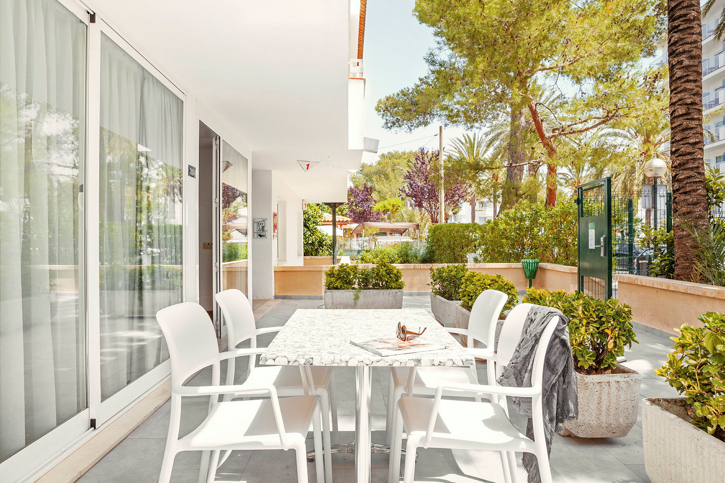 Utendørsområde med bord og stoler på en steinbelagt terrasse, omgitt av grøntområder. (AI-generert tekst)