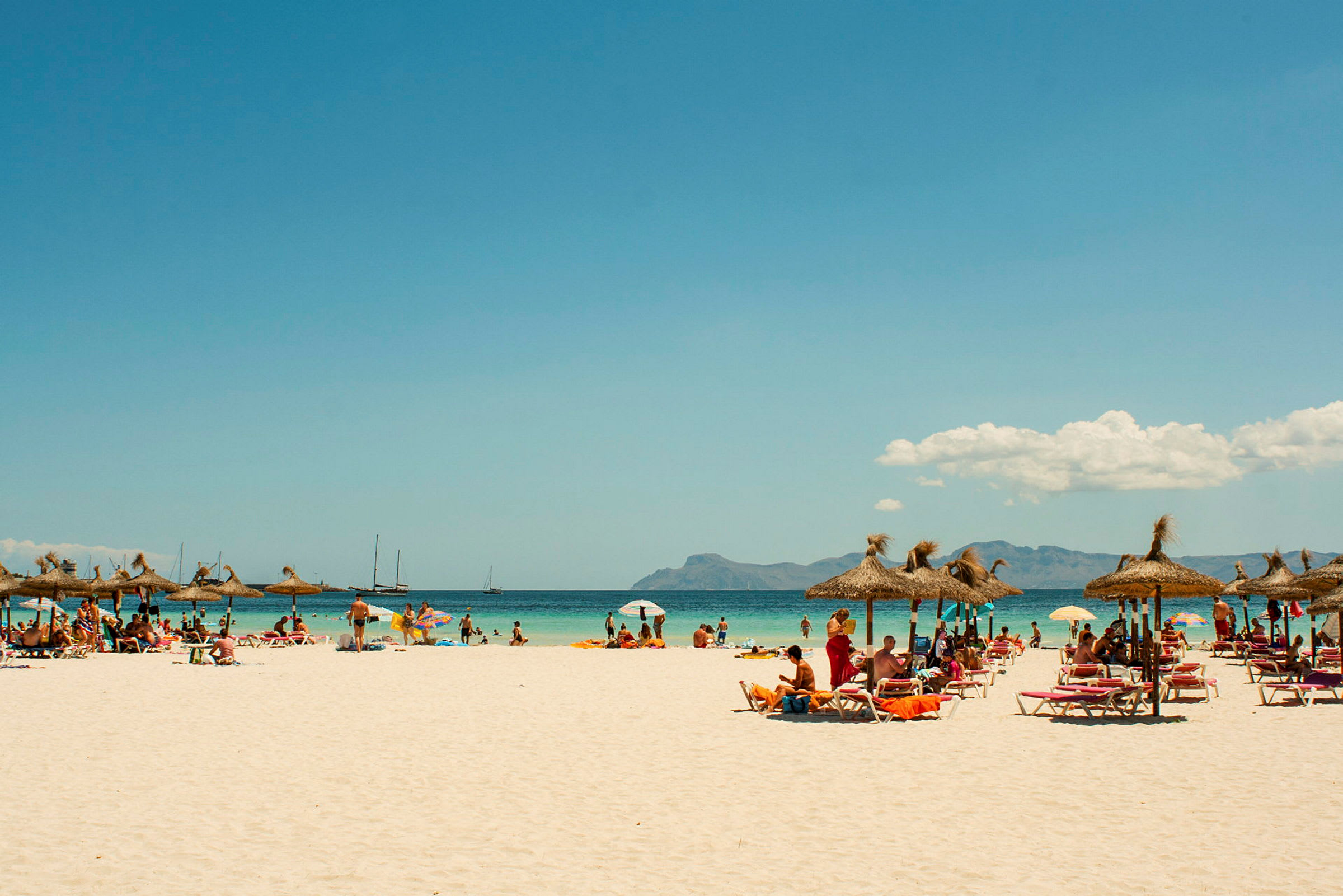 Strand med parasoller og solsenger, mennesker bader og nyter solen. (AI-generert tekst)