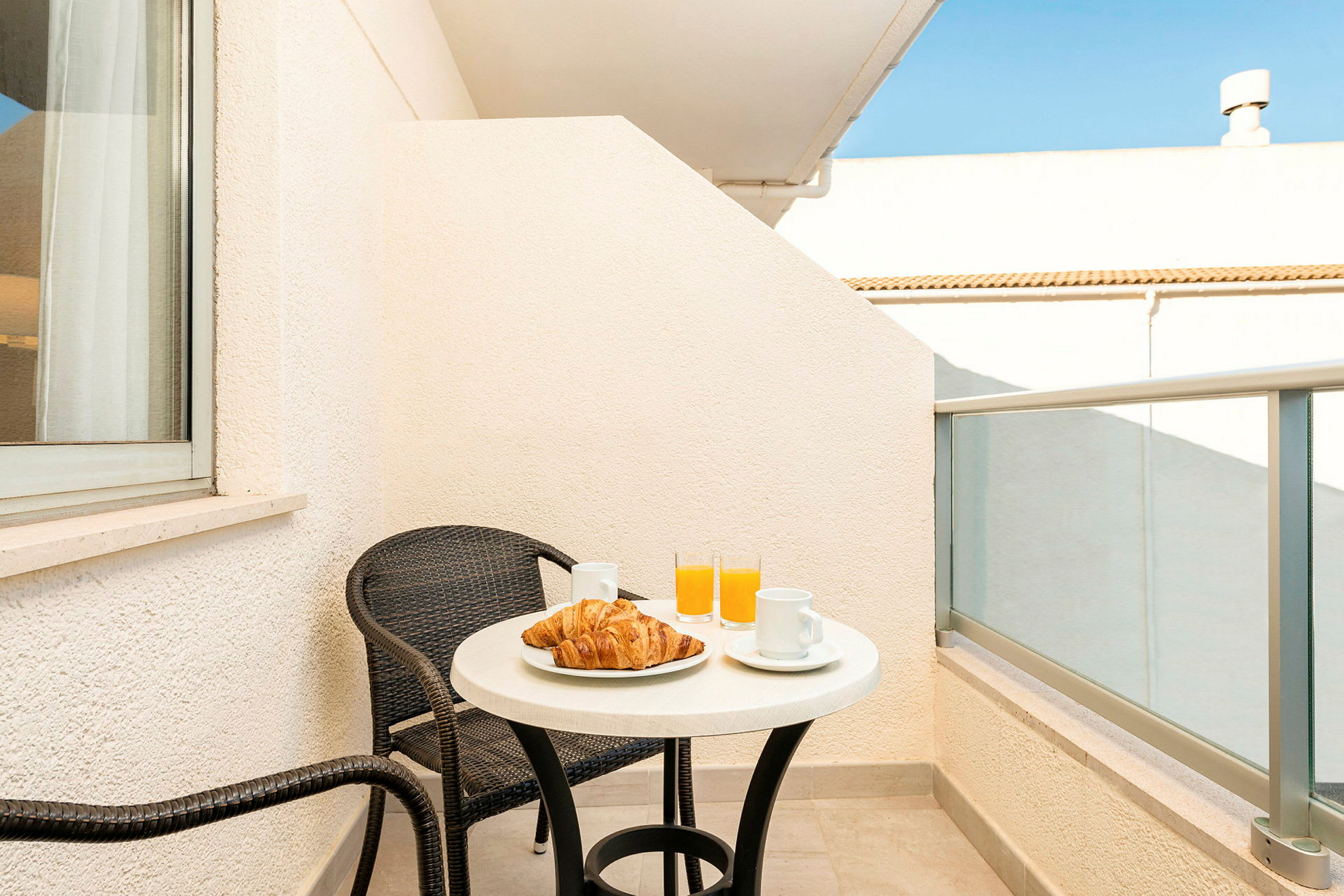 En balkong med et bord, to stoler, croissant, kaffekopper og glass med appelsinjuice. (AI-generert tekst)