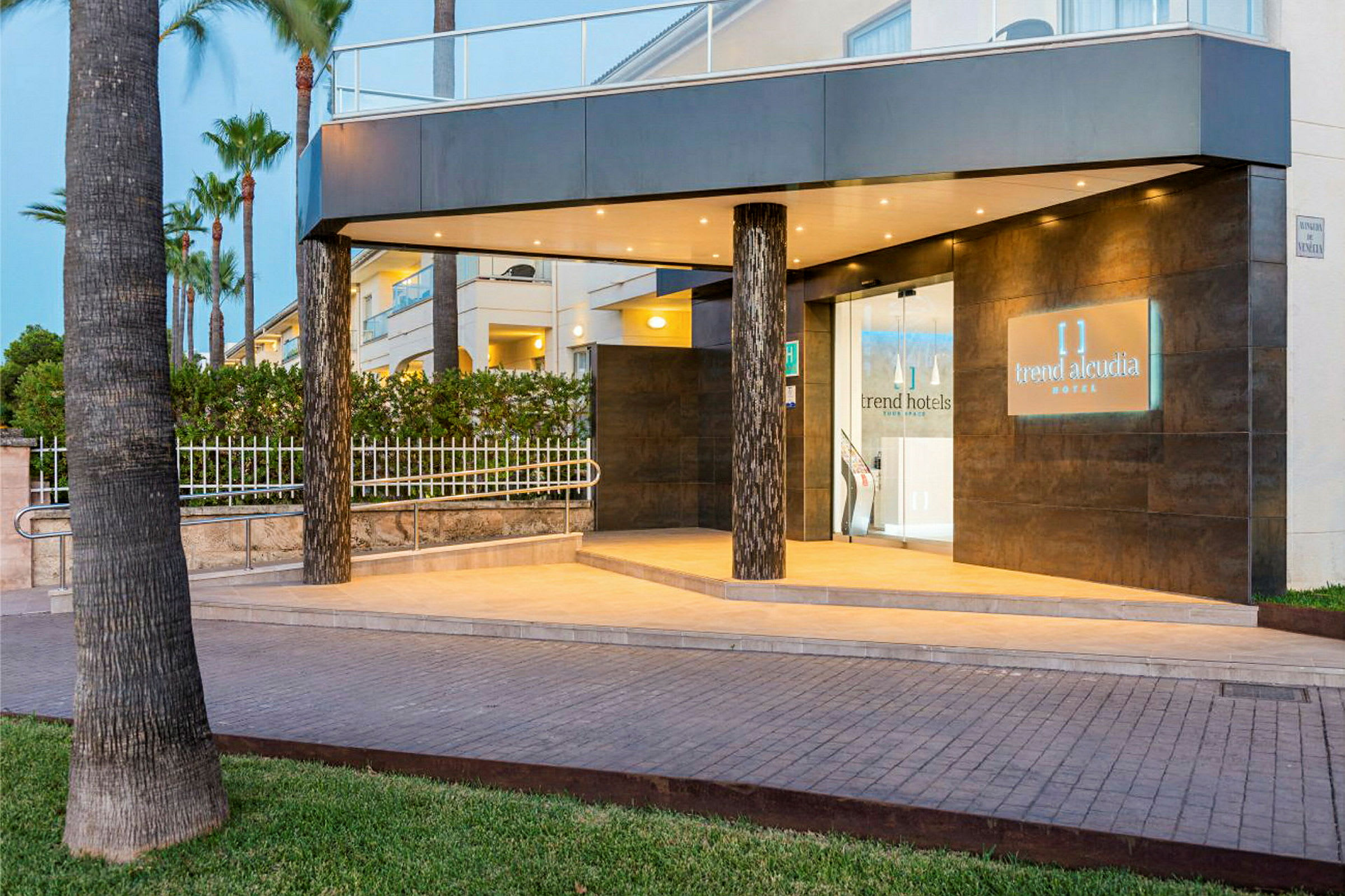 Inngangen til et hotell med belysning og navnet 'Trend Alcudia Hotel' på et skilt. (AI-generert tekst)