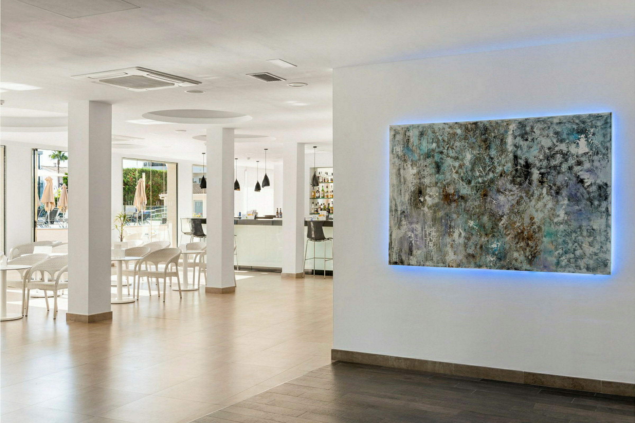 Interiør fra et moderne kaféområde. På veggen henger et kunstverk med blått lys bak. (AI-generert tekst)