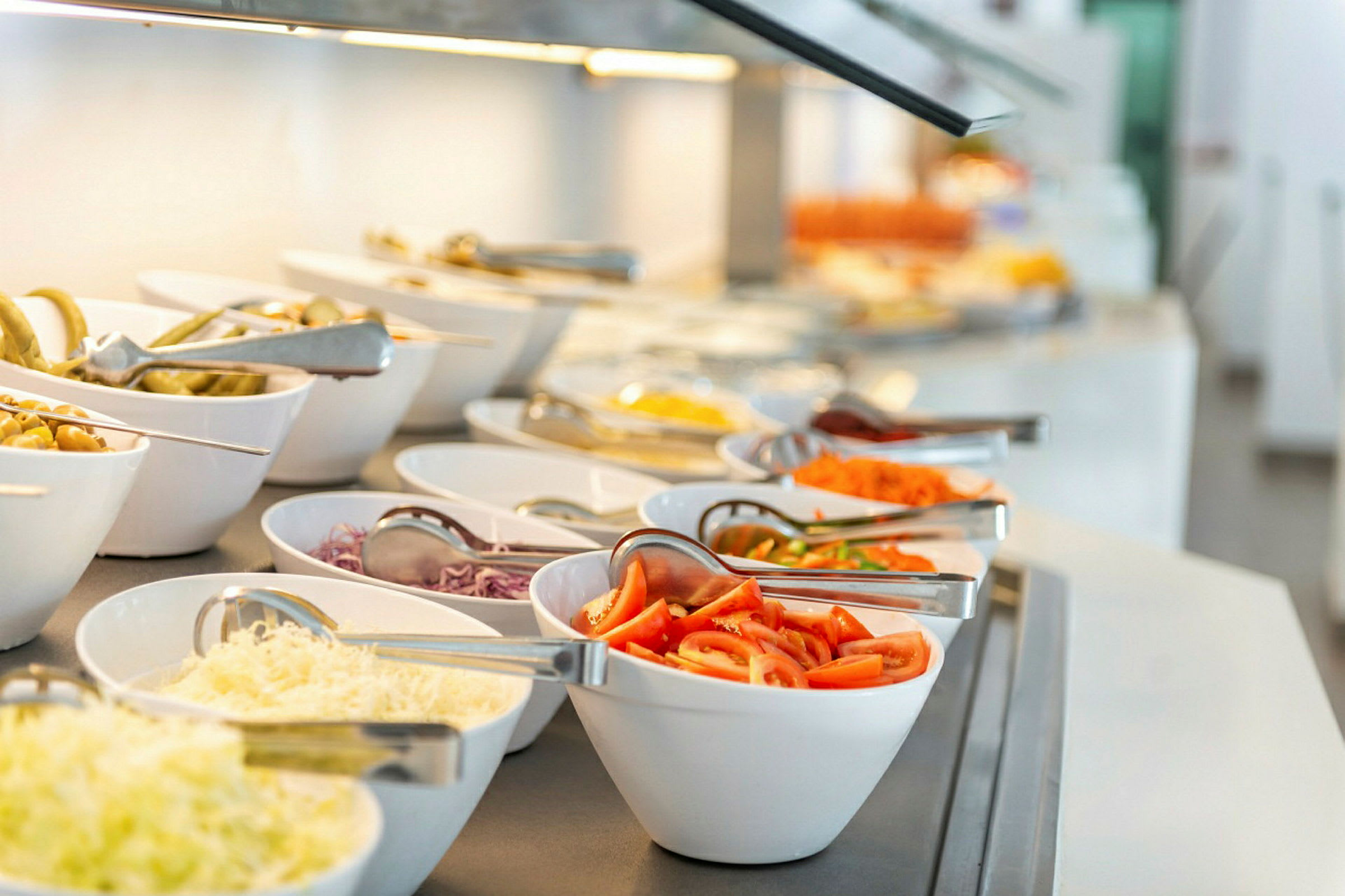 Buffet med ulike salatingredienser i hvite skåler. (AI-generert tekst)