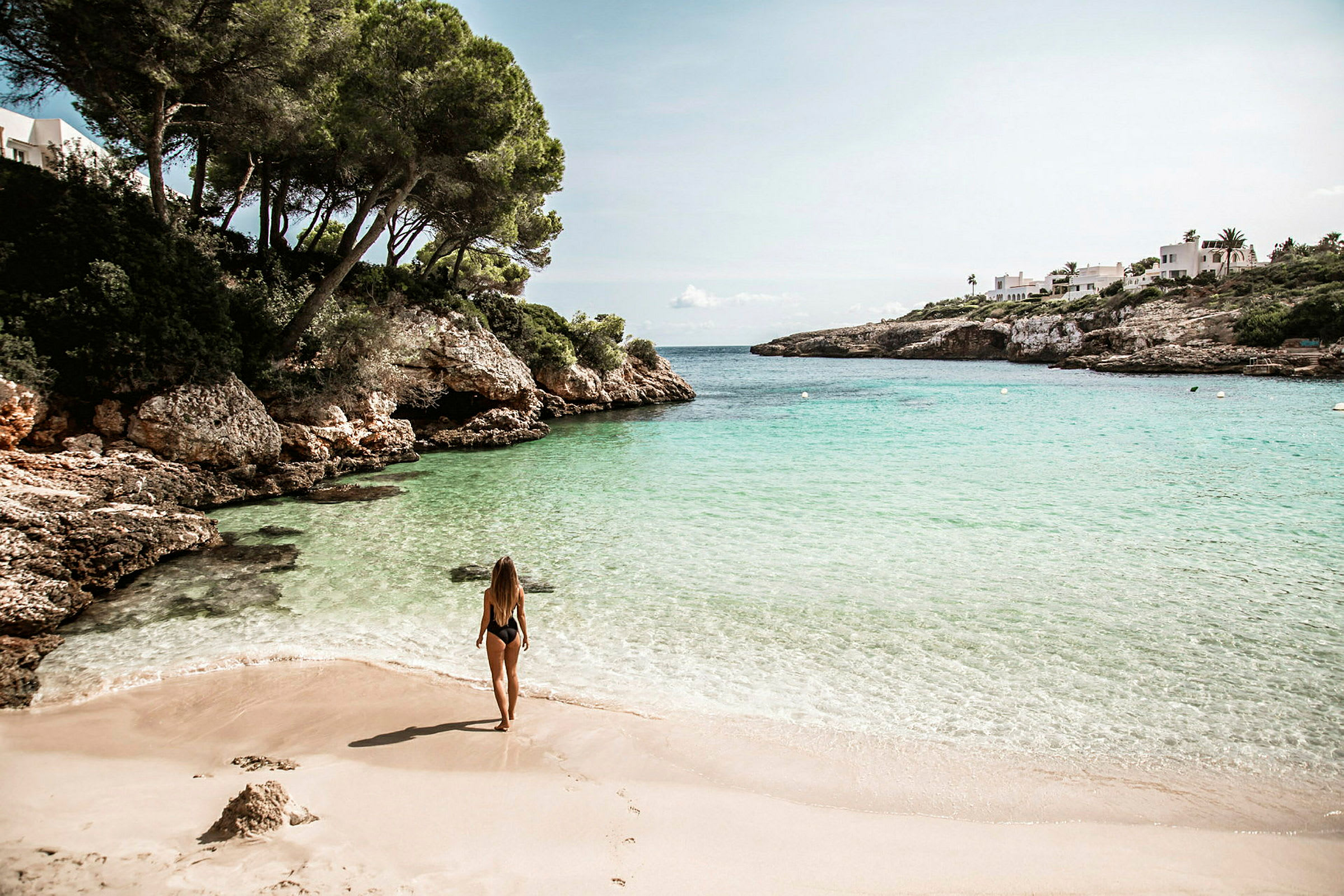 En kvinne står på en sandstrand ved en vik med klipper og klart vann. (AI-generert tekst)