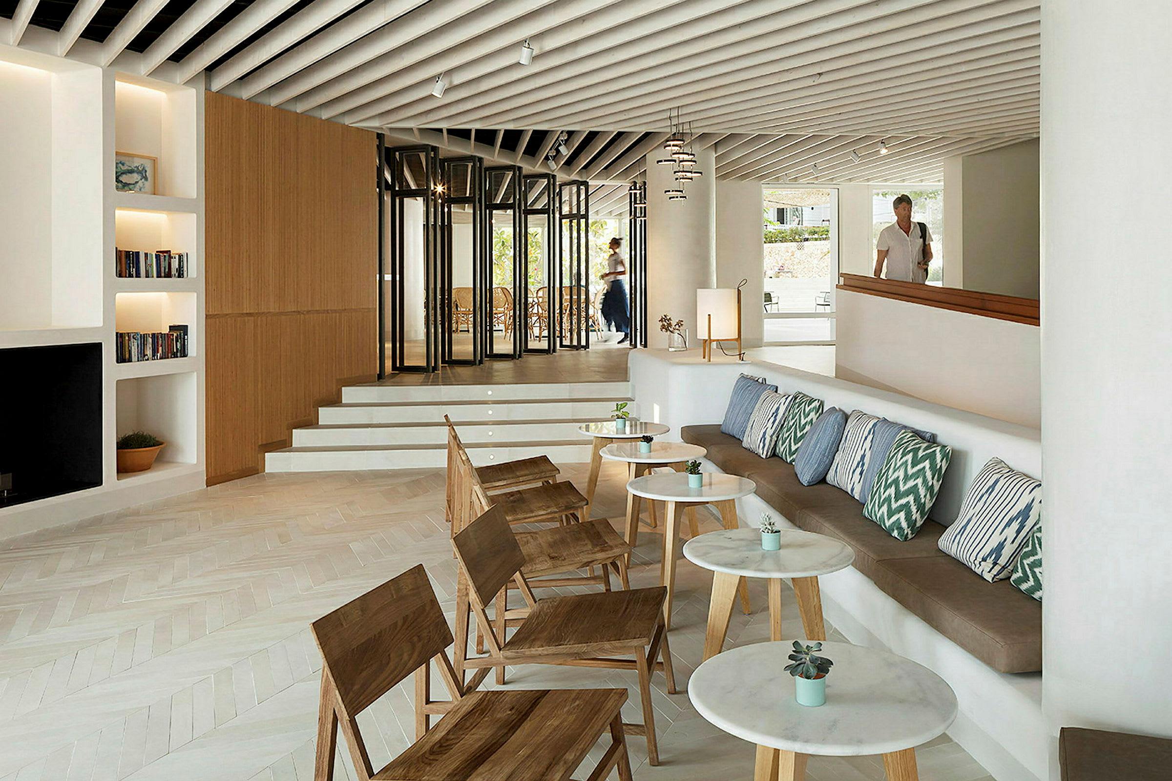 Et moderne hotellrom med sittegruppe, trestoler, puter og små bord. (AI-generert tekst)