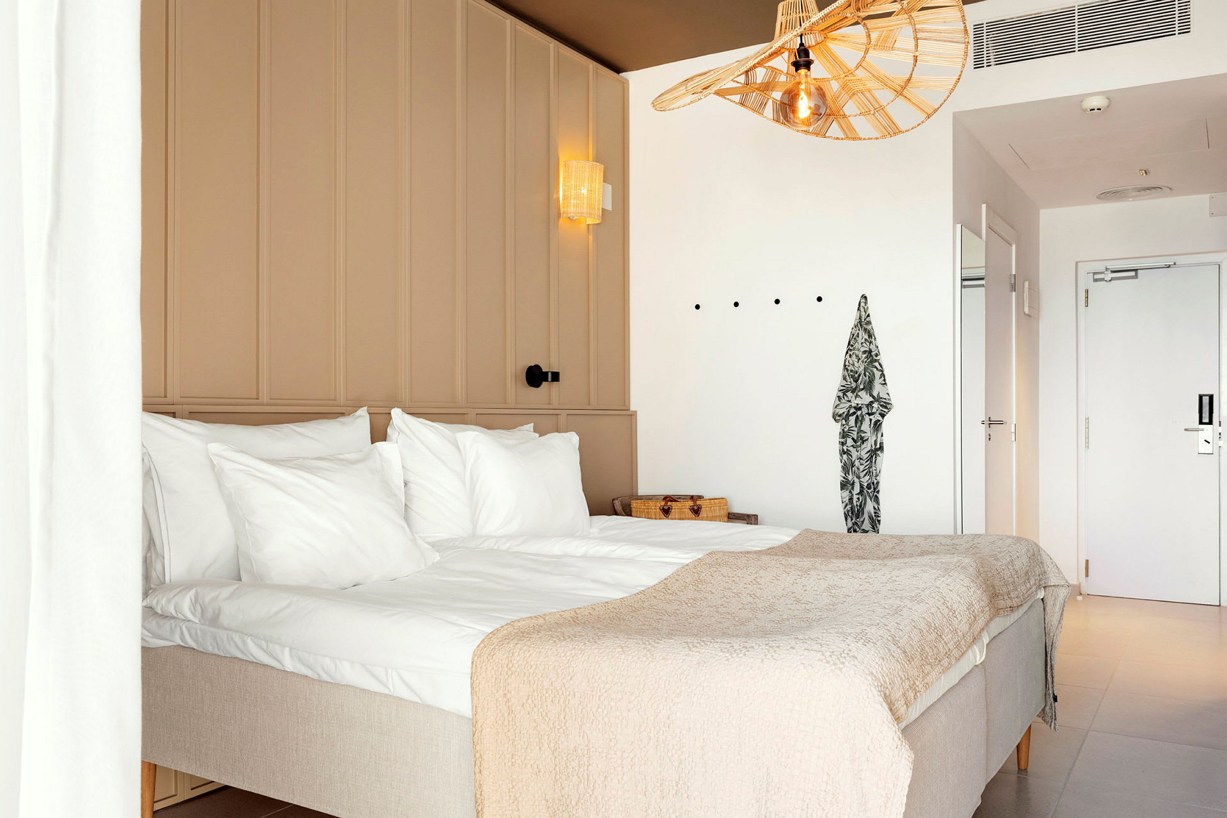 Et hotellrom med en dobbeltseng, hvite vegger og lys innredning. (AI-generert tekst)