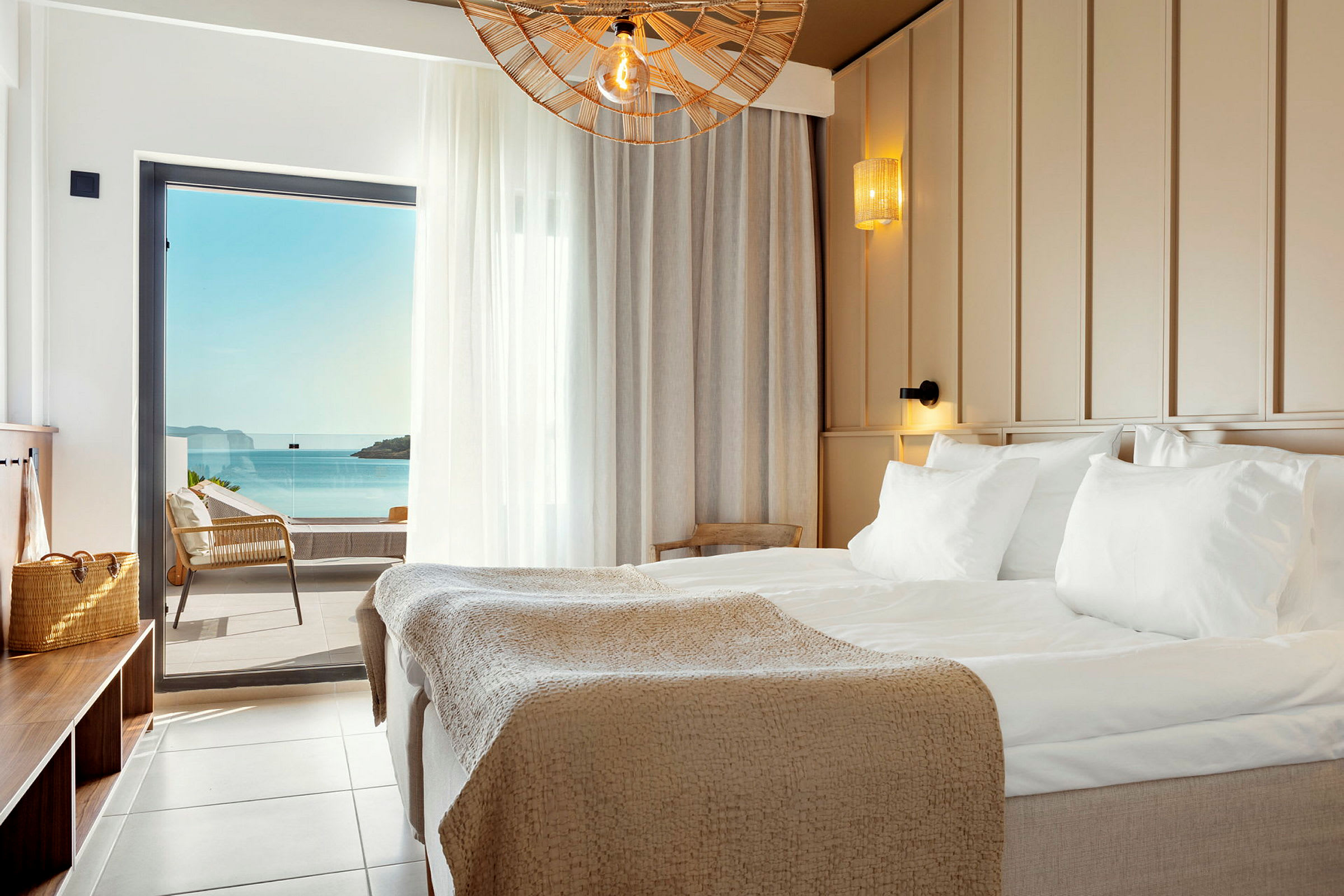 Et hotellrom med en stor seng og havutsikt gjennom en balkongdør. (AI-generert tekst)