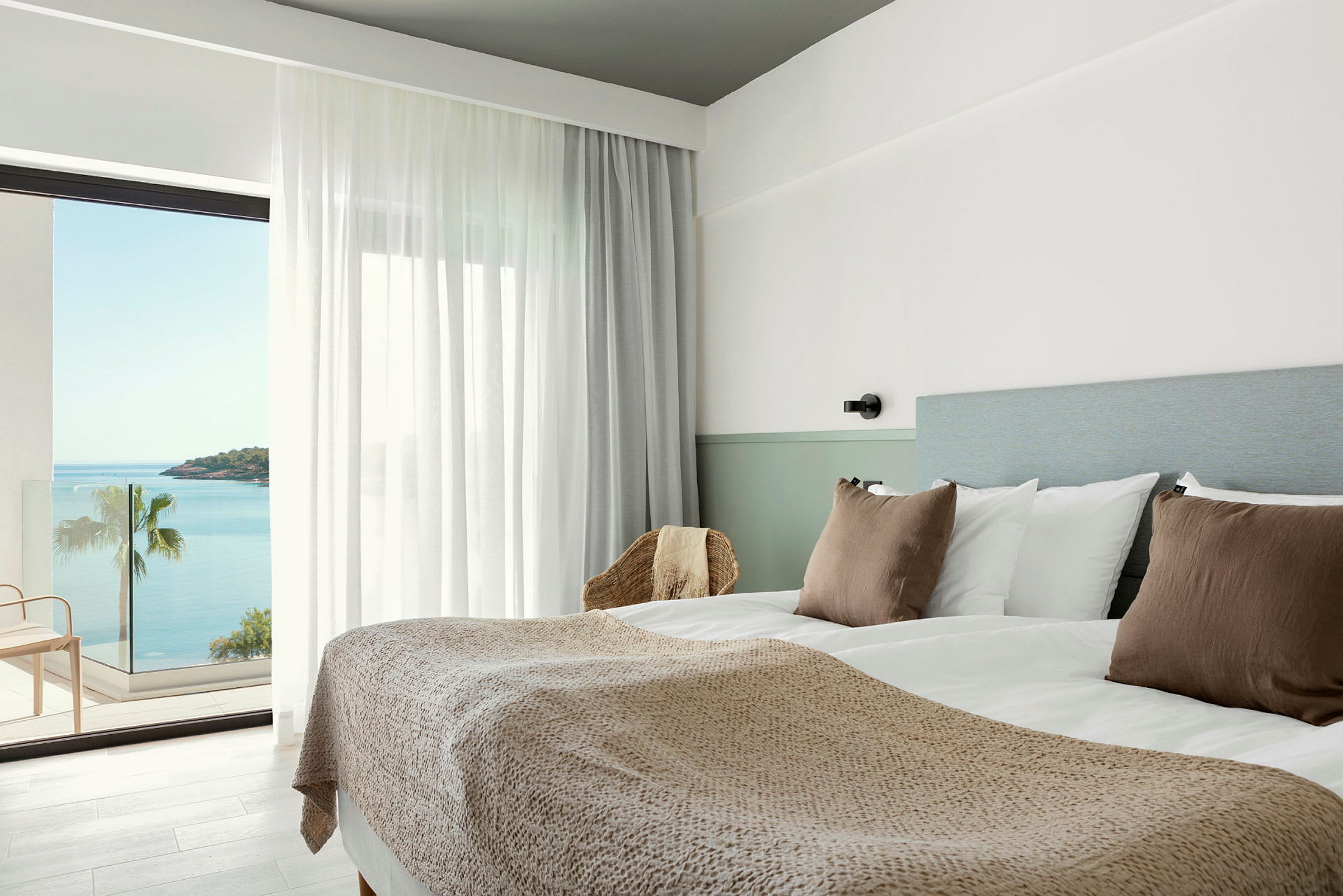 Hotellrom med dobbeltseng, lyse farger og havutsikt fra balkongen. (AI-generert tekst)