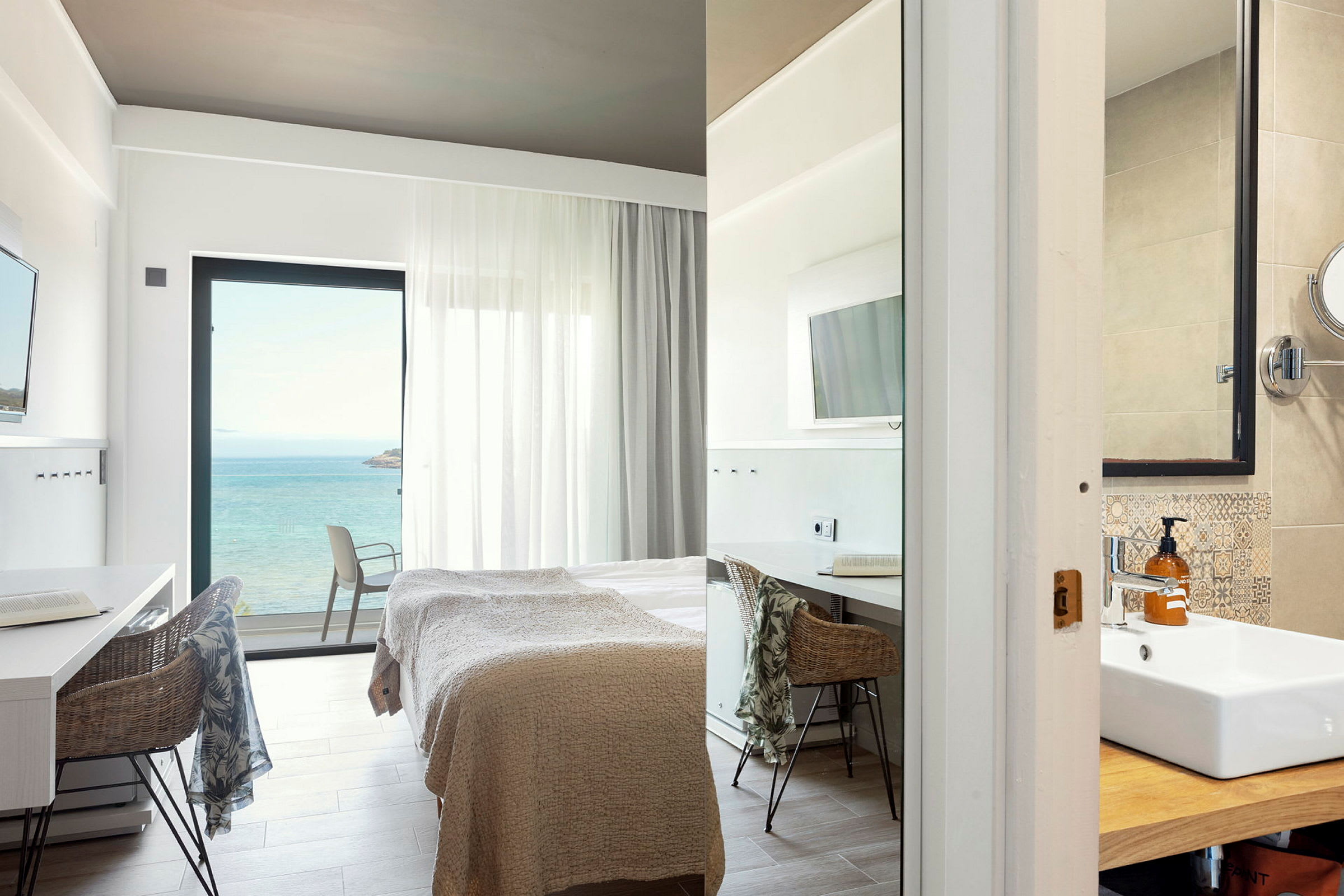 Moderne hotellrom med havutsikt, seng og arbeidsområde samt del av bad. (AI-generert tekst)