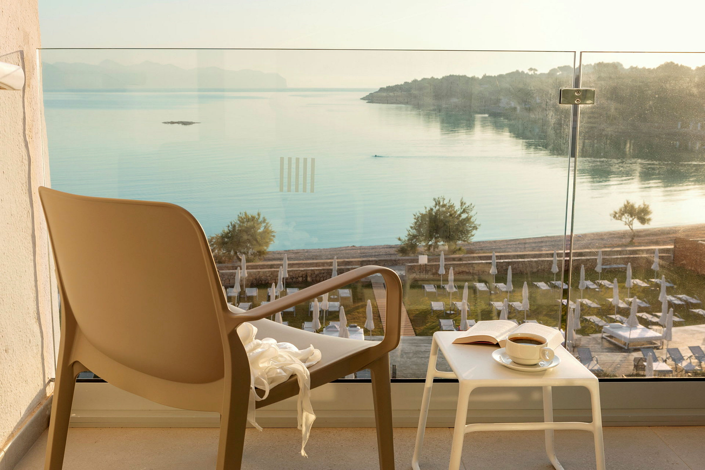 Stol og bord med en kopp kaffe og bok på en terrasse med utsikt over havet. (AI-generert tekst)