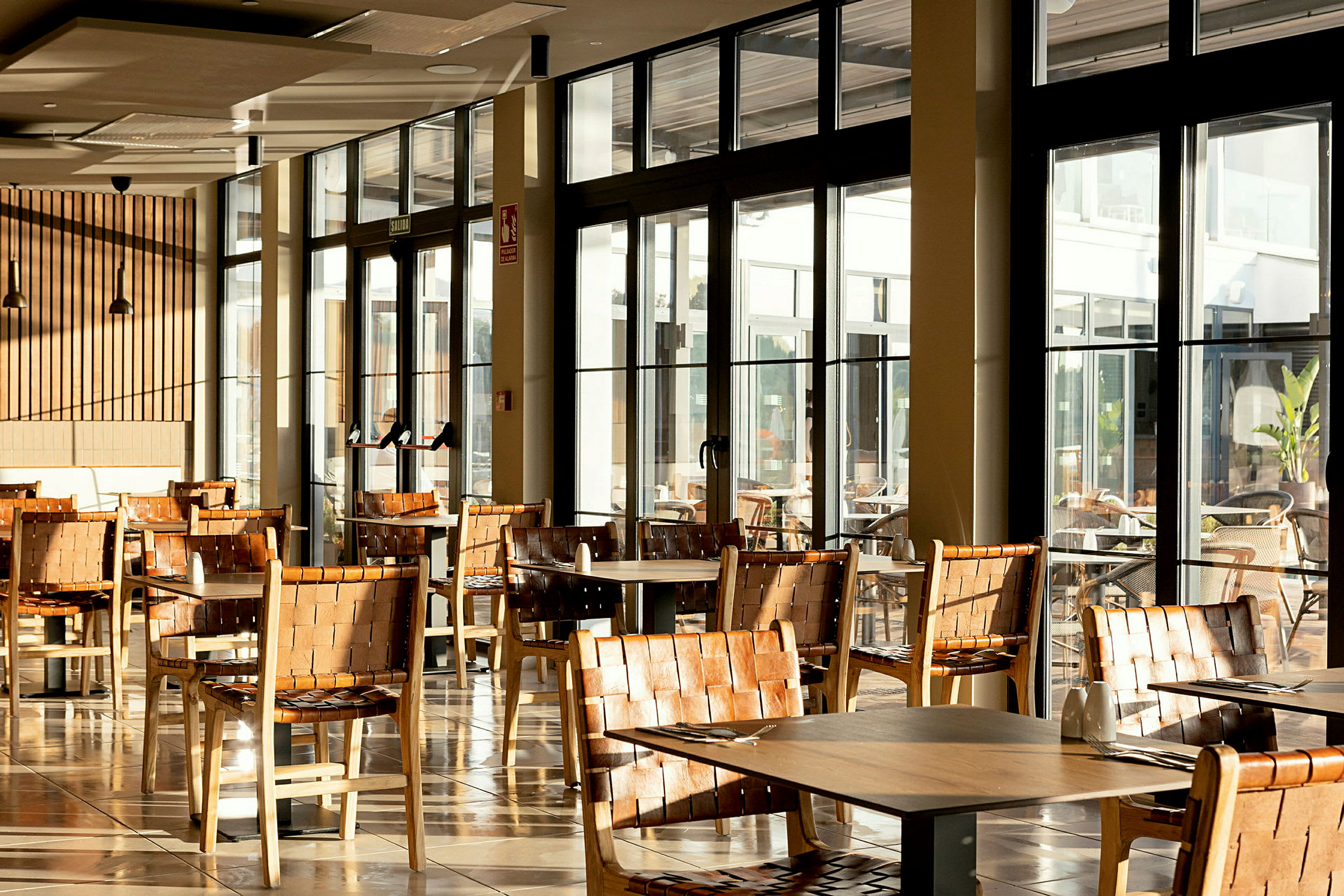 Restaurantområde med bord og stoler i tre, store glassvinduer med utsikt. (AI-generert tekst)