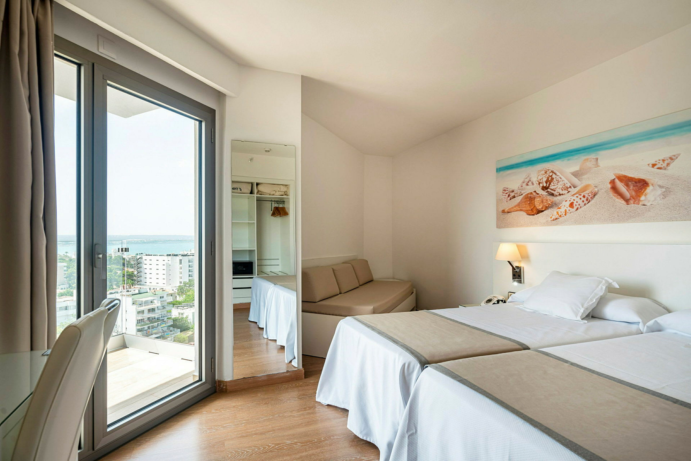 Et hotellrom med to enkeltsenger, et lite bordområde og en glassdør med utsikt ut. (AI-generert tekst)
