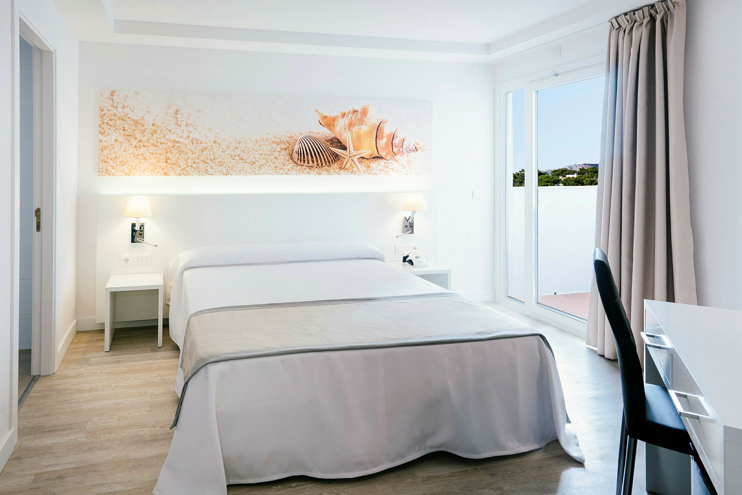 Et hotellrom med dobbeltseng, hvitt og beige interiør, dekorasjon med skjell over sengen. (AI-generert tekst)