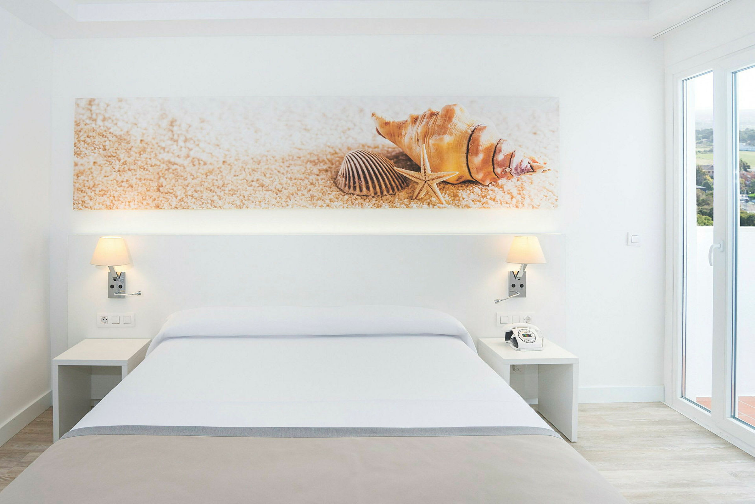 Moderne hotellrom med en stor seng og dekorativt bilde som viser skjell over. (AI-generert tekst)