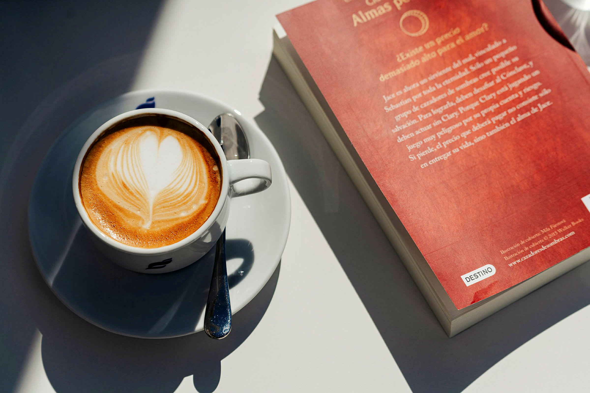 En kopp cappuccino med hjerteformet lattekunst ved siden av en bok med rødt omslag. (AI-generert tekst)