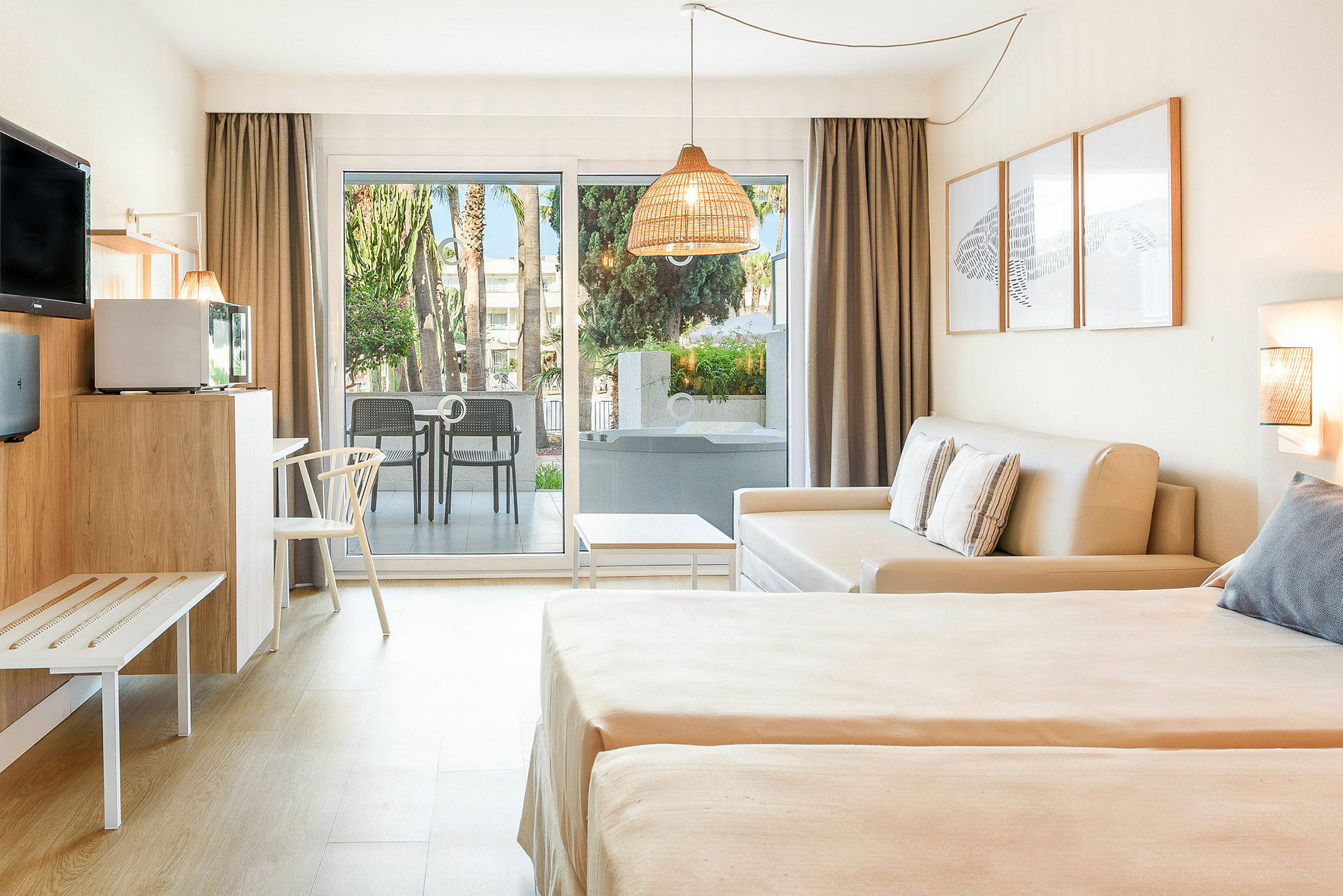 Et hotellrom med lys innredning, en sovesofa, to senger og en terrasse med utsikt over grøntområder. (AI-generert tekst)
