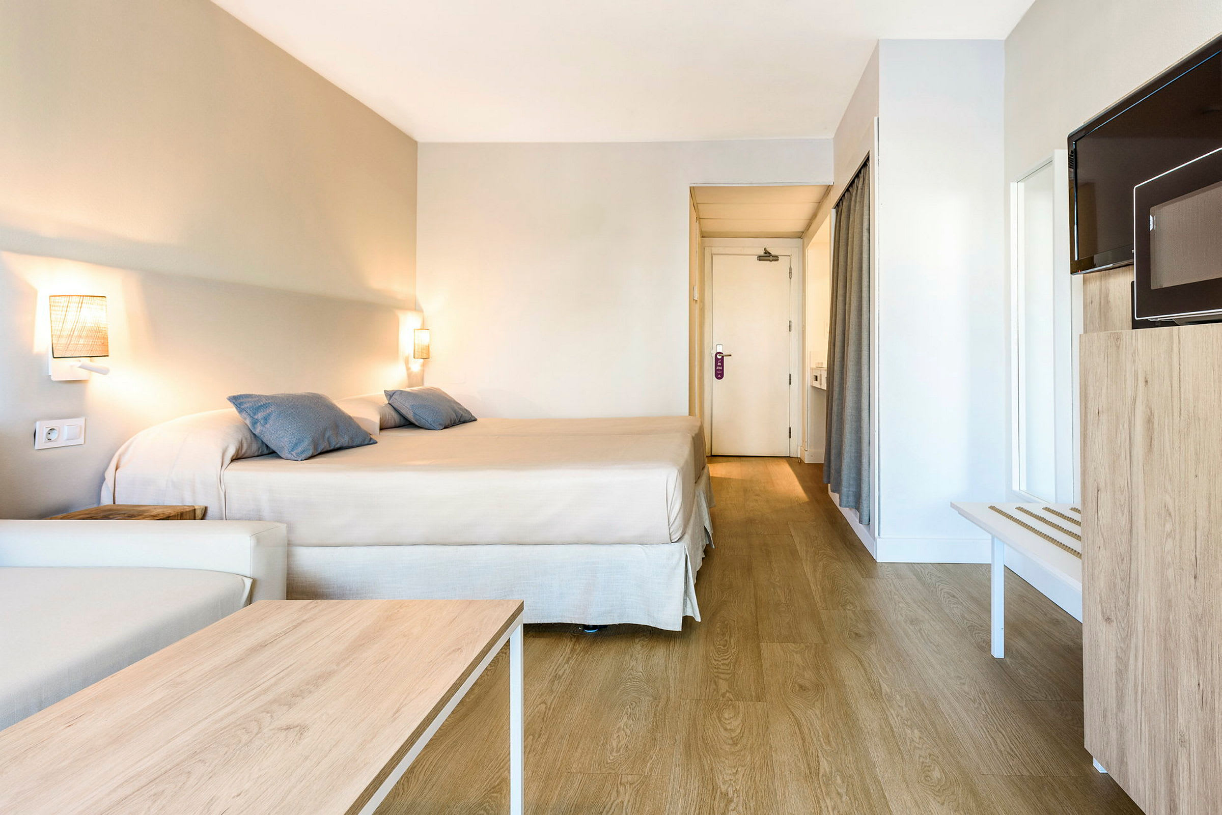 Hotellrom med en dobbeltseng, en sofa, et trebord, en TV og en dør til badet. (AI-generert tekst)