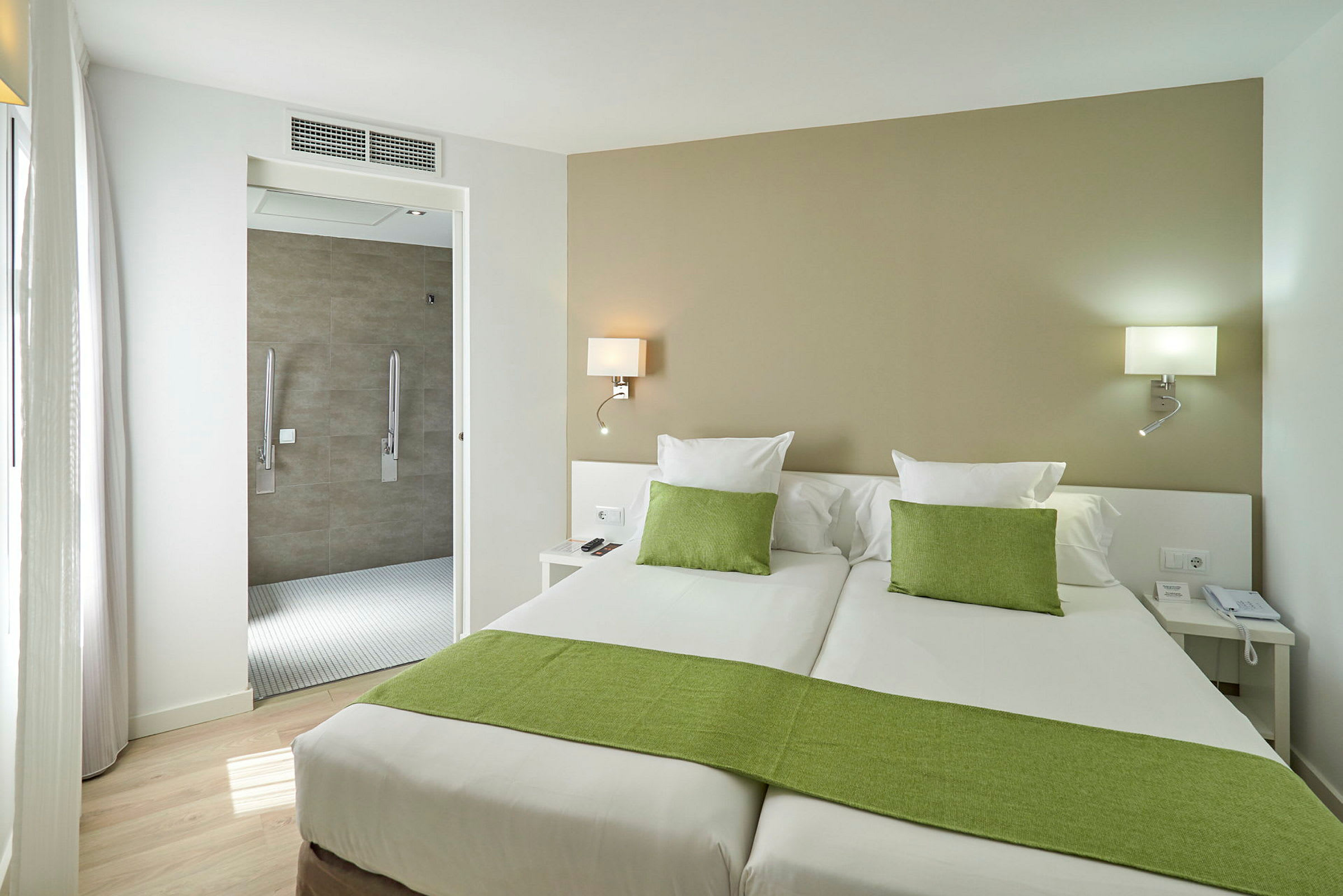 Hotellrom med to enkeltsenger, grønt sengetøy og en åpning mot badet. (AI-generert tekst)