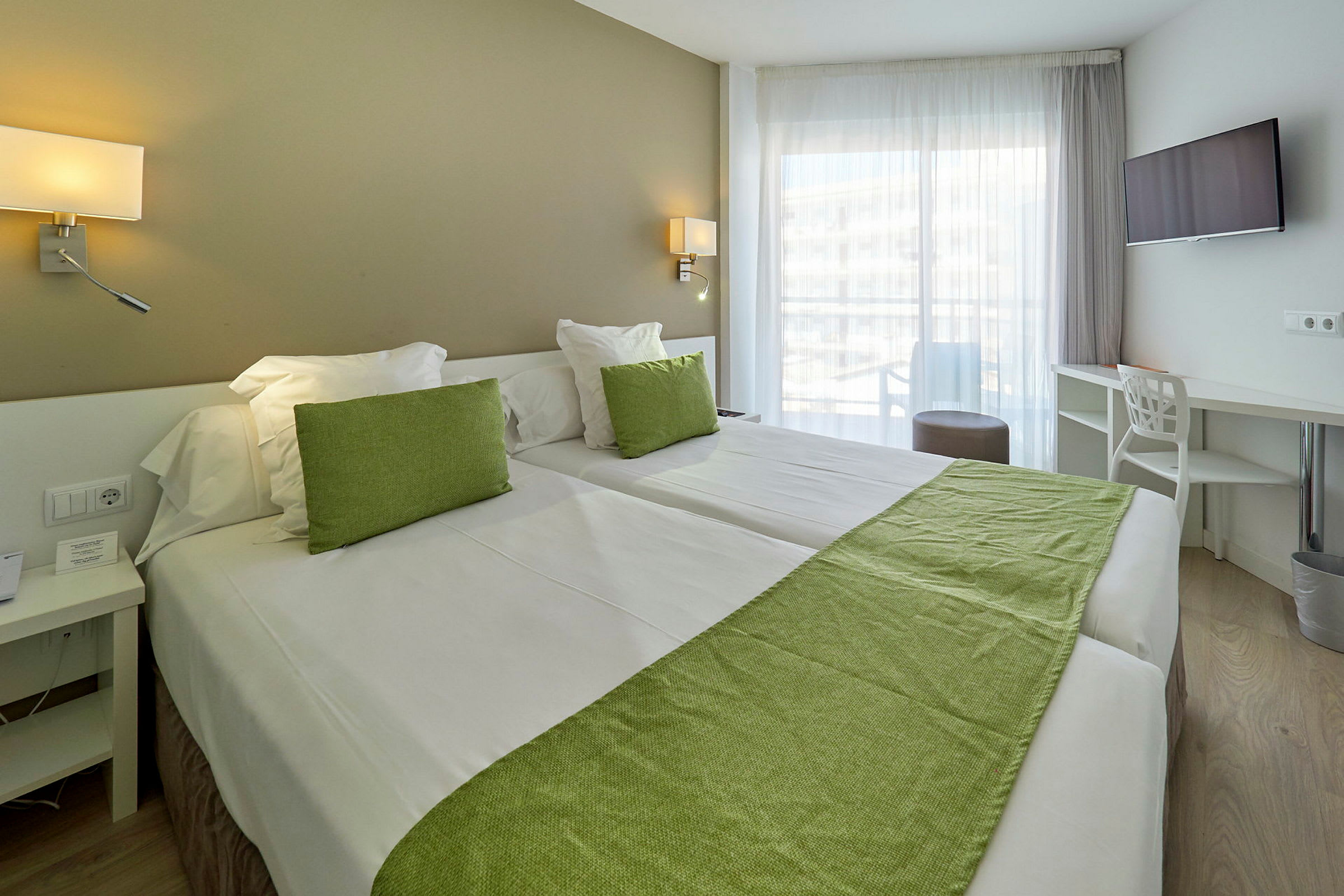 Hotellrom med to senger, grønn dekorasjon og store vinduer. (AI-generert tekst)