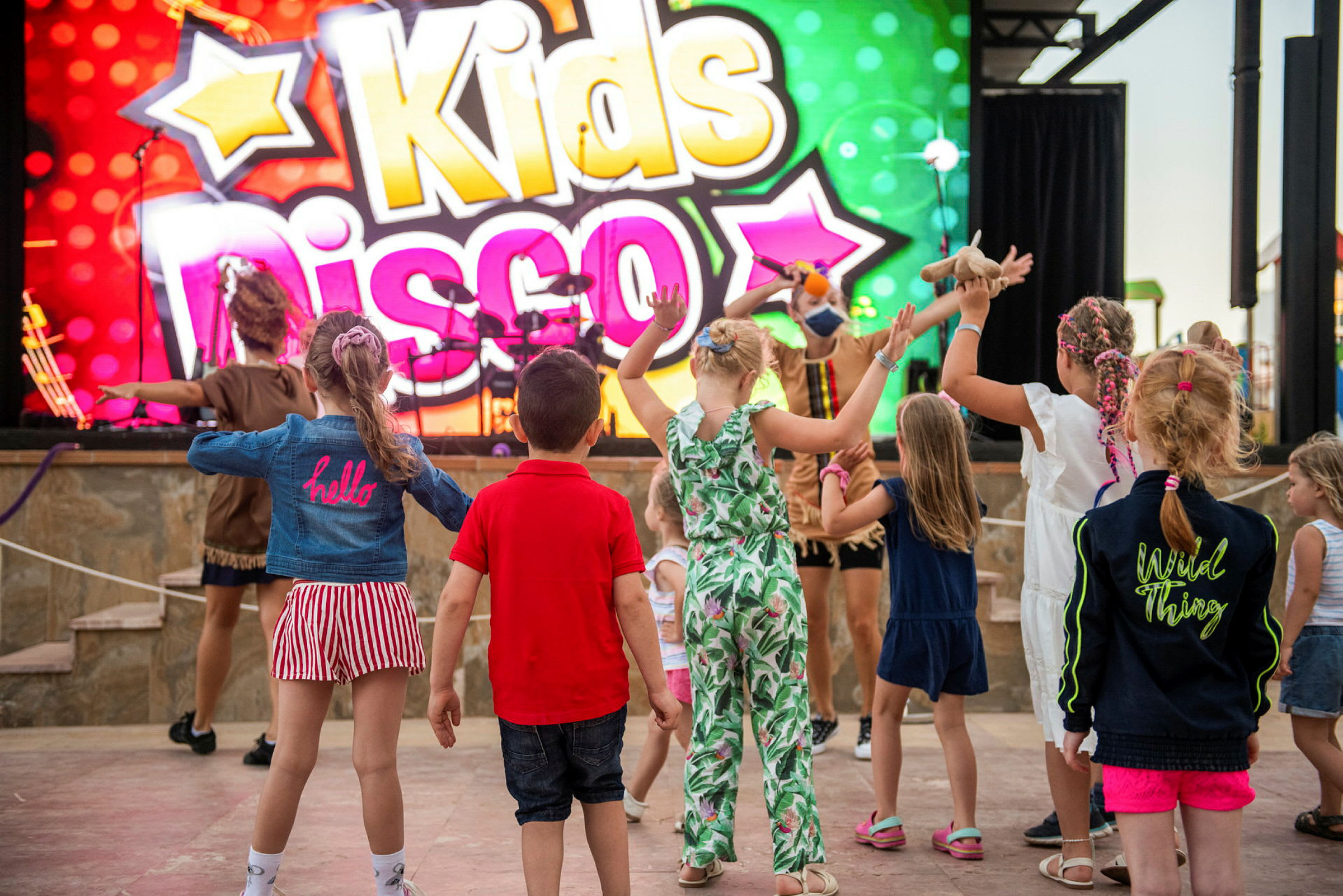 Barn som danser foran et fargerikt skilt med teksten 'Kids Disco'. (AI-generert tekst)