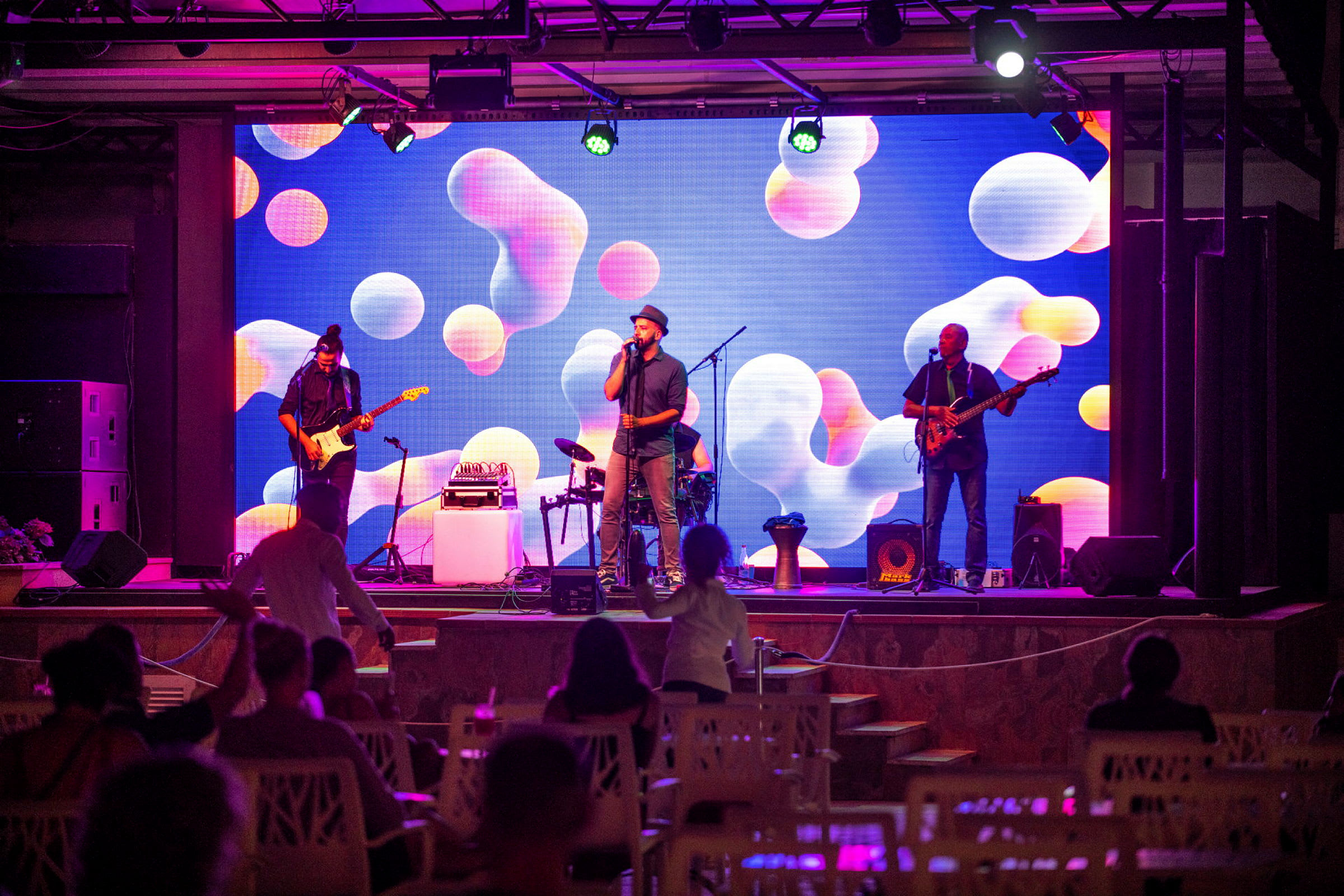 En musikkonsert med et band på scenen og en fargerik bakgrunn. (AI-generert tekst)