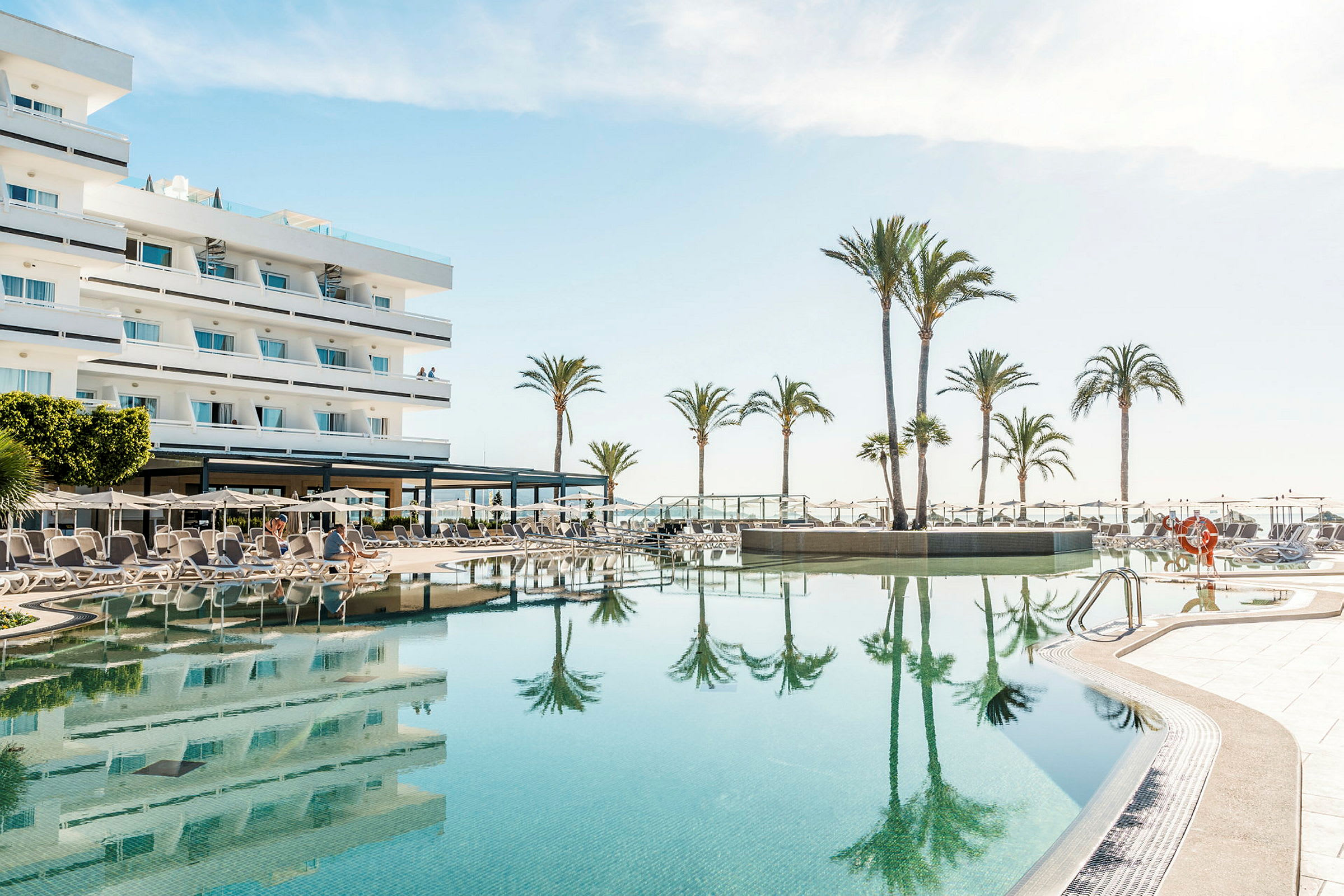 Hotell med svømmebasseng og solsenger ved en solfylt strand. (AI-generert tekst)